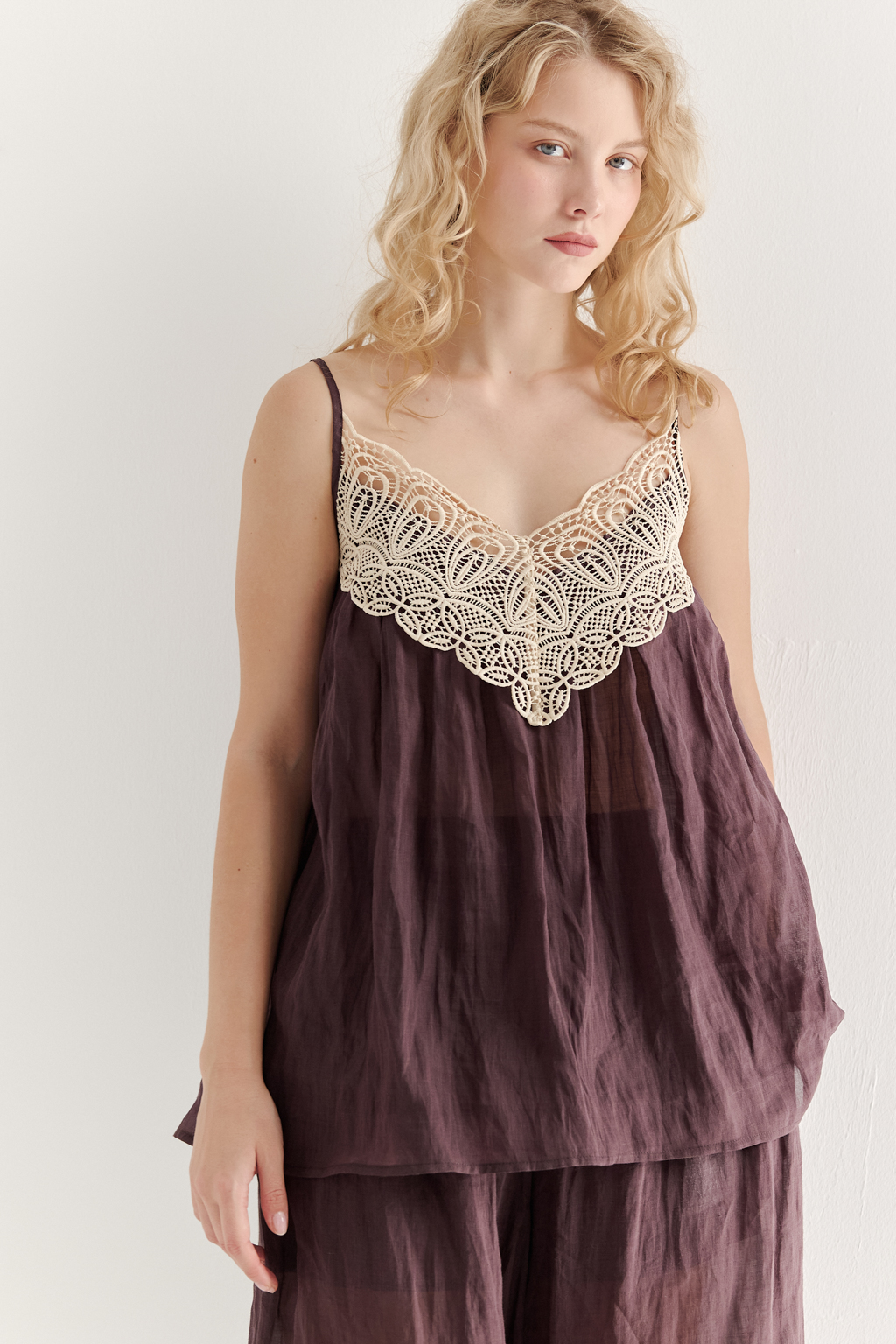 Топ-трапеция, выполненный из стопроцентной крапивы с крэш-эффектом благородного коричневого оттенка, украшен отделкой из кружевного гипюра нежного бежевого цвета. Кружевная деталь изысканно располагается на передней части изделия. Деталь переда топа настрочены на кружево со сборкой, по верхнему срезу спинки предусмотрена резинка, обеспечивающая оптимальную посадку. Бретели топа регулируются. Топ представляет собой идеальный комплект с брюками из крапивы, льна или хлопка, создавая гармоничный и стильный образ