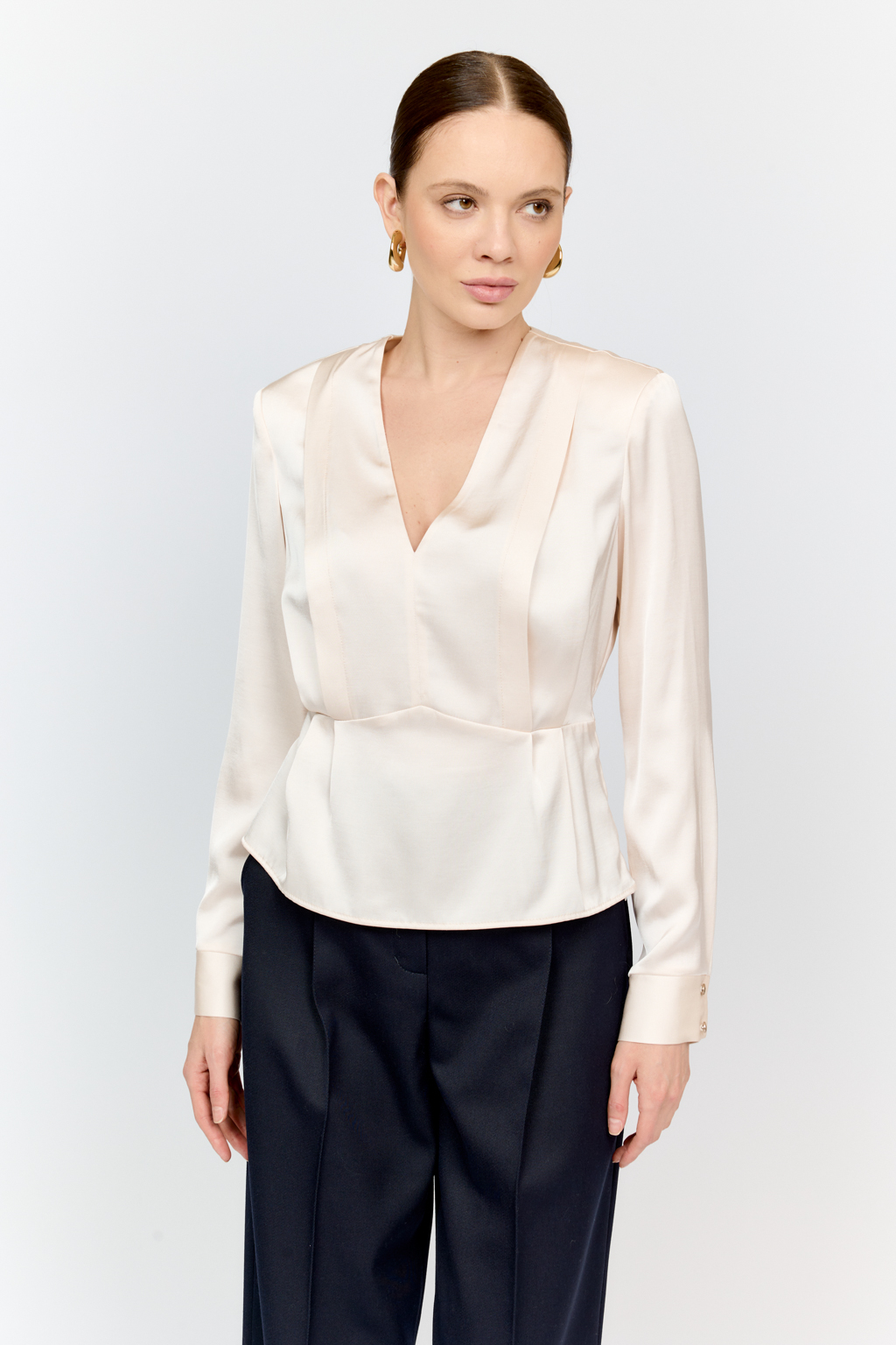 Блуза с глубоким V-образным вырезом горловины и фигурным резом по линией груди, на которой заложены глубокие складки из вискозы с атласной фактурой.