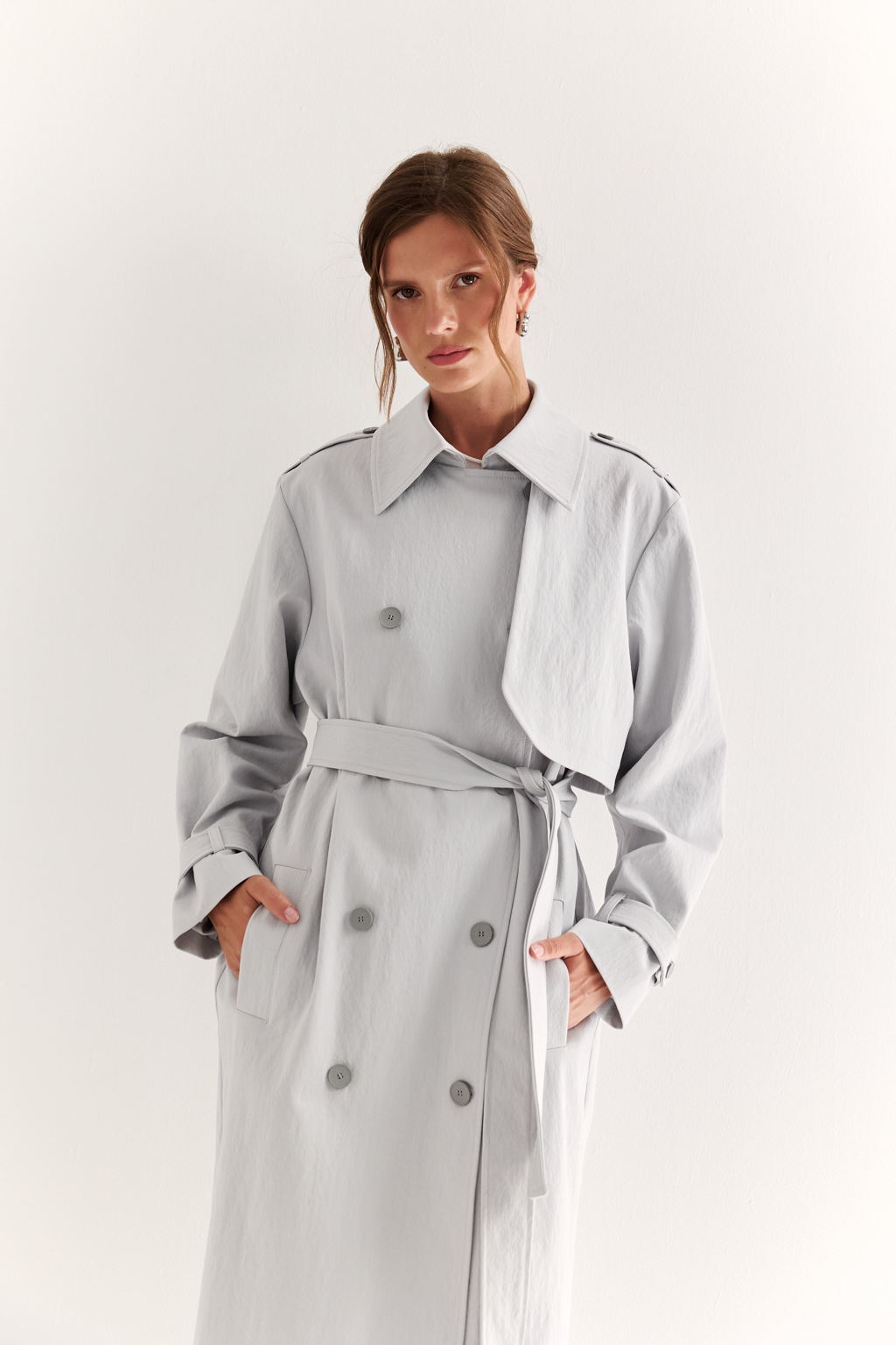 Плащ двубортный прямого силуэта длиной макси с расширенной линией плеча и отлётными кокетками по полочке и спинке. Приталивается завязывающимся поясом.