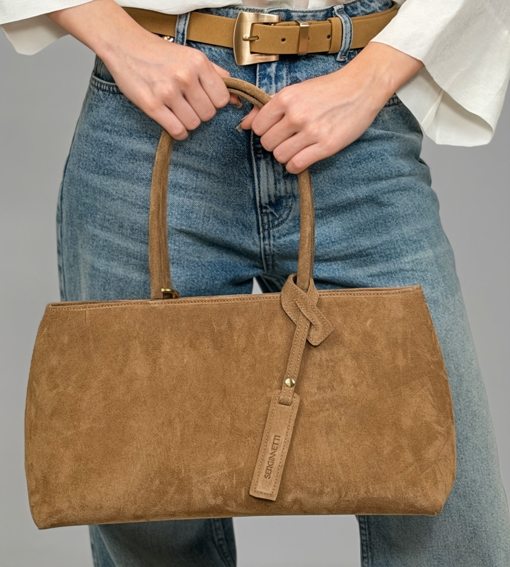 Сумка-тоут выполнена из натуральной замши. Аксессуар закрывается на металлическую молнию,имеет удобные ручки и брелок. Размеры сумки: 45*21*5,8 см.