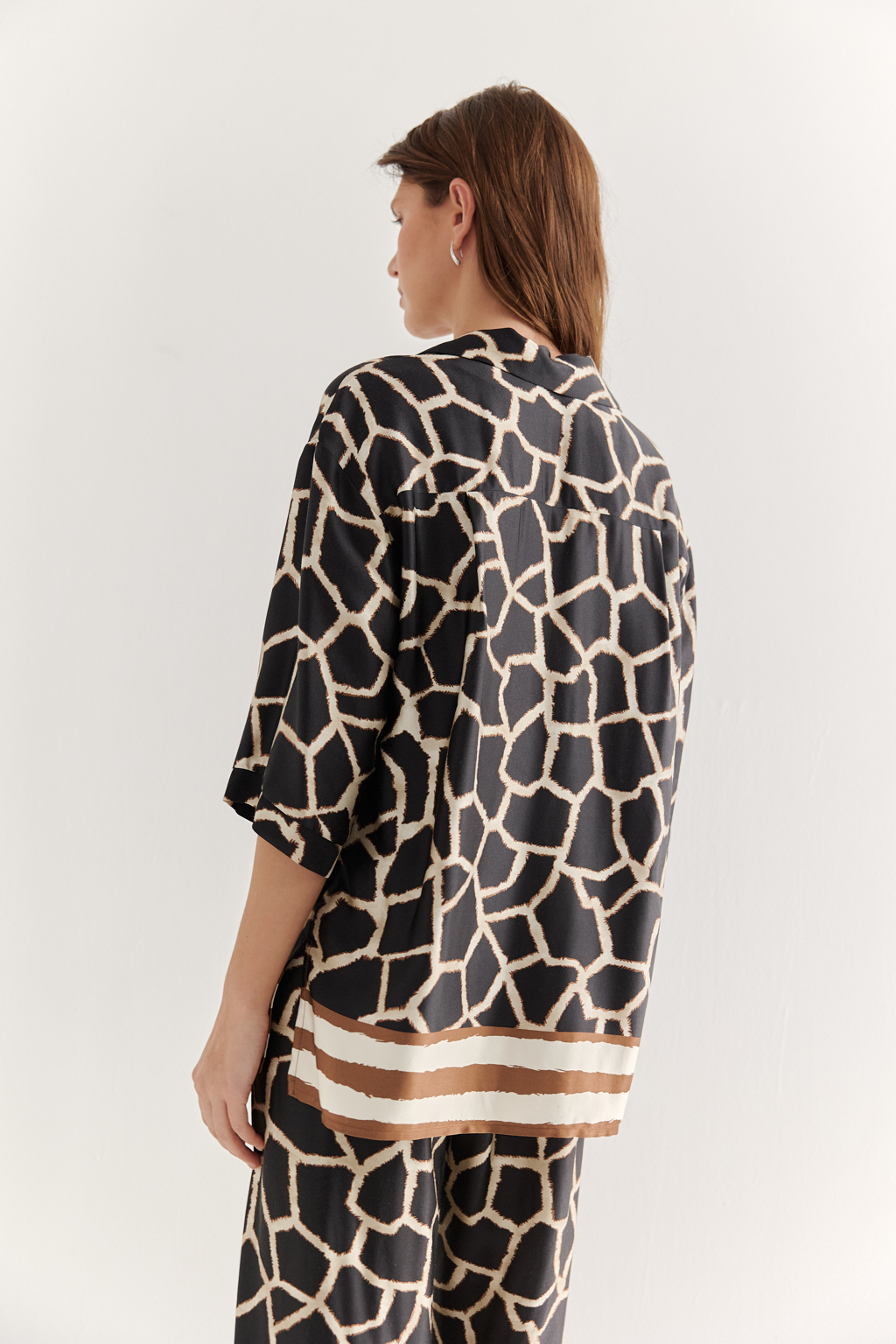 Блуза с коротким рукавом, выполненная из полированной вискозы с шелковистой текстурой, украшена эксклюзивным анималистическим принтом, разработанным дизайнерами бренда. Отложной воротник, застежка на пуговицы по переду и деликатные разрезы в боковых швах подчеркивают изысканный силуэт. Уникальный бордюр завершает принт по низу изделия, добавляя акцент. Блуза, сочетающая в себе непринужденный стиль и комфорт, идеально подходит в качестве второго слоя к пижамным брюкам из той же коллекции, создавая гармоничный и расслабленный образ.