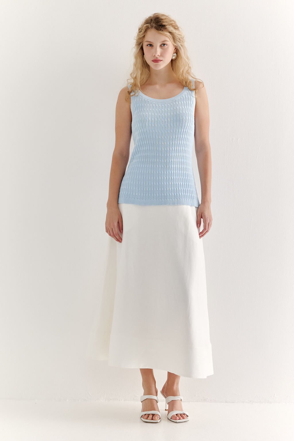 Фактурный топ-майка прилегающего силуэта из вискозной пряжи связана косами, проймы и горловина отделаны вязанными кантами. Цвет – голубой.