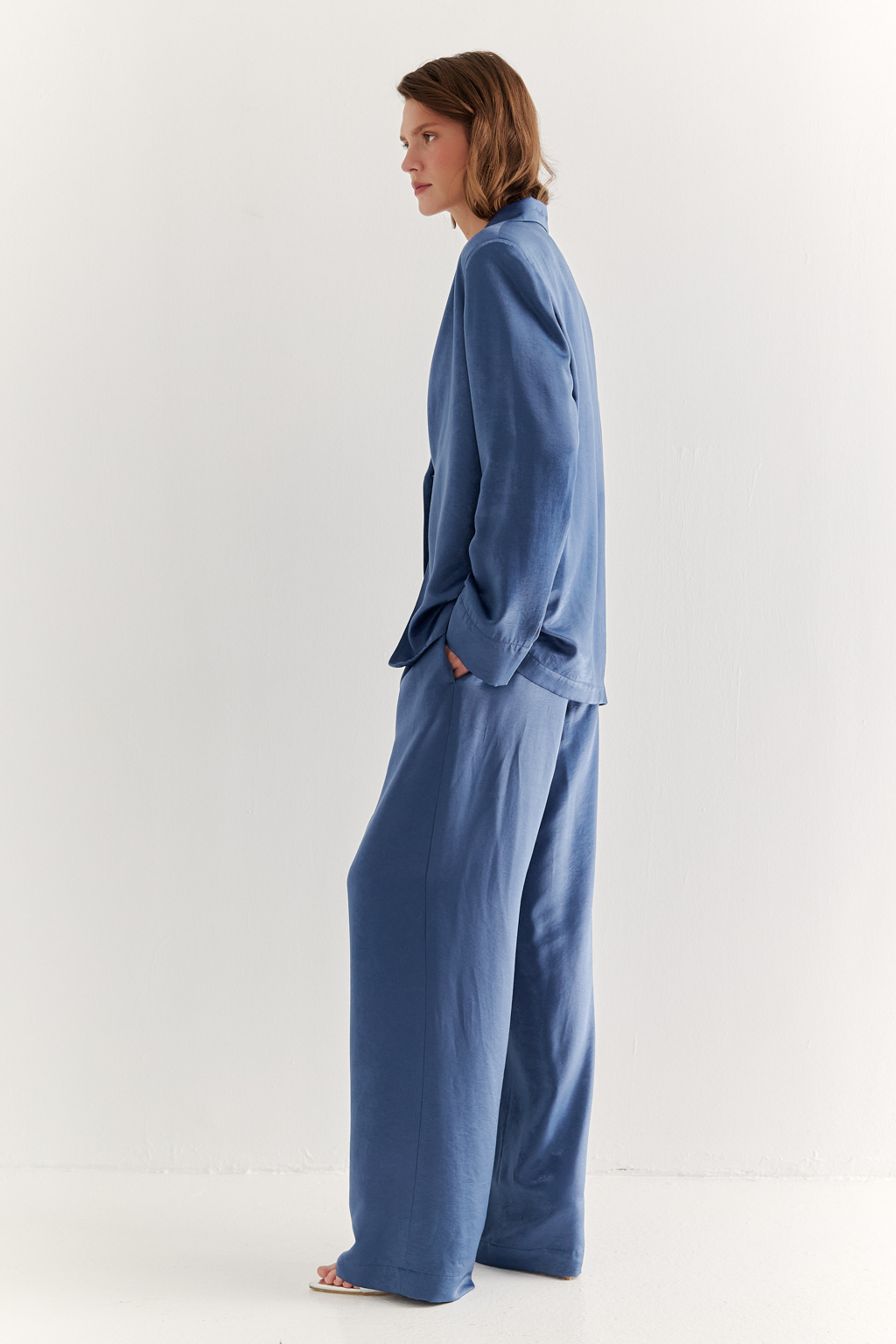 Брюки, широкие и прямые по всей длине, выполнены из струящегося атласа, что является воплощением актуального тренда на мягкий комфорт. Стильный цвет классического денима и фактура ткани, напоминающая мокрый шёлк, определяют ключевое направление в моде: создание атмосферы комфорта, пронизанной заботой и бережным отношением к себе. Брюки оснащены удобными карманами и эластичным поясом, обеспечивающими максимальный комфорт и удобство. Идеальным дополнением к этим брюкам станут топ и жакет в пижамном стиле, позволяющие создать элегантный монохромный образ.