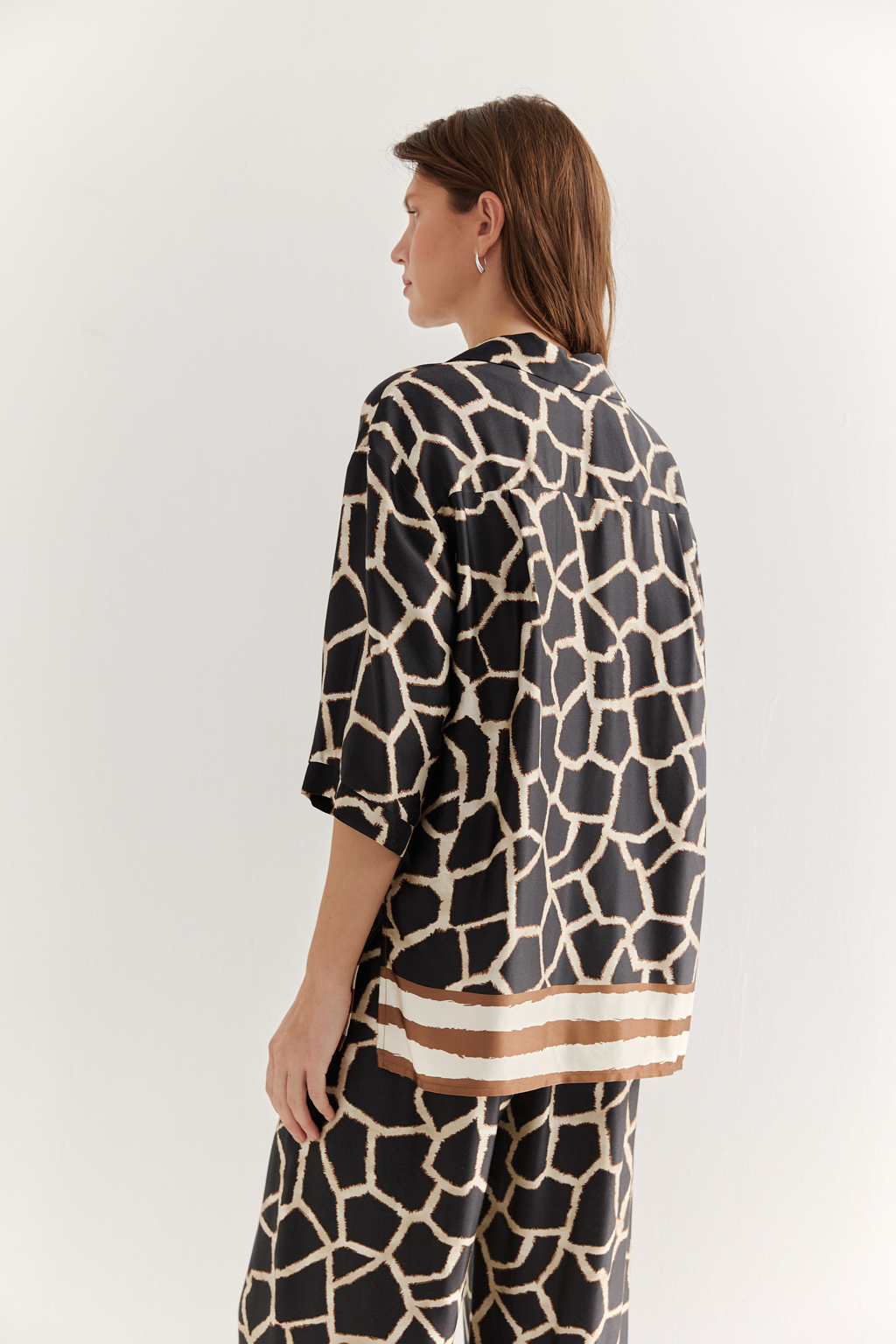 Блуза с коротким рукавом, выполненная из полированной вискозы с шелковистой текстурой, украшена эксклюзивным анималистическим принтом, разработанным дизайнерами бренда. Отложной воротник, застежка на пуговицы по переду и деликатные разрезы в боковых швах подчеркивают изысканный силуэт. Уникальный бордюр завершает принт по низу изделия, добавляя акцент. Блуза, сочетающая в себе непринужденный стиль и комфорт, идеально подходит в качестве второго слоя к пижамным брюкам из той же коллекции, создавая гармоничный и расслабленный образ.