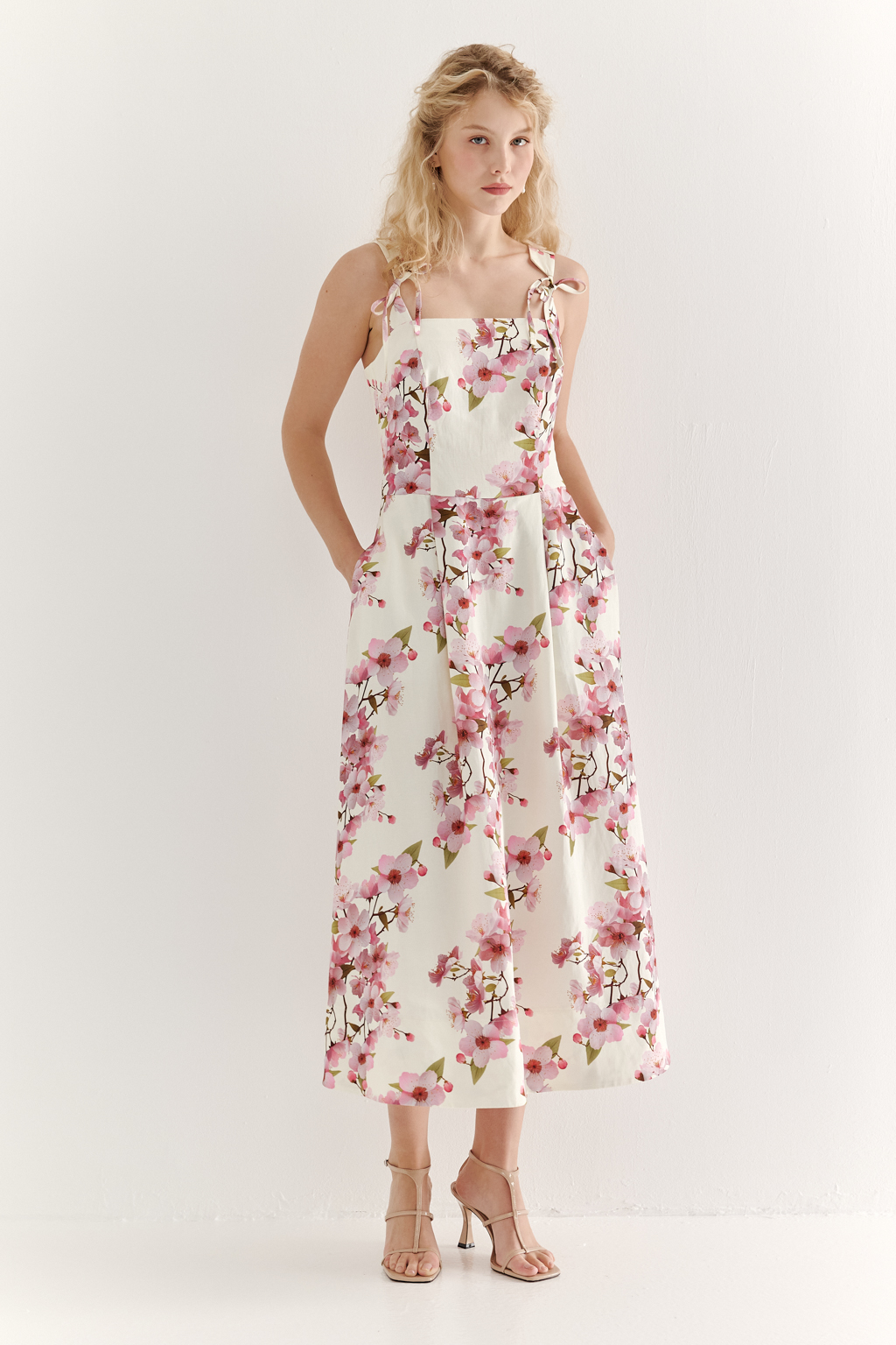 Платье-сарафан полуприлегающего силуэта выполнено из плотной пластичной ткани в основе которой волокна вискозы и льна. Лиф-бандо, акцент на линию талии и юбка полусолнце формируют изящный Х-образный силуэт. Особую утонченность платью придают бретели сложной формы, изящно завязывающиеся на шнуры. Эластичная деталь на спинке платья, собранная на нити-стрейч, и застежка-молния в боковом шве обеспечивают комфортную и превосходную посадку по фигуре. Ключевой деталью, выделяющей этот наряд, является эксклюзивный принт, разработанный в дизайн-бюро бренда. В этом принте нежные розовые цветы сакуры и молочный оттенок фона образуют гармоничное, элегантное сочетание, рождающее ощущение красоты и утонченности.