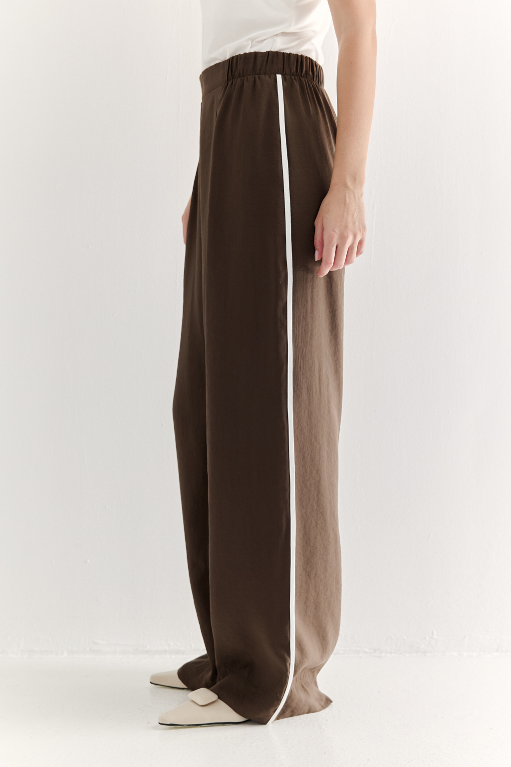 Эти широкие брюки свободного кроя, выполненные из мягкого модала насыщенного шоколадно-коричневого оттенка. Бархатистая текстура ткани, созданная благодаря особой обработке, дарит неповторимое ощущение нежности, тактильно напоминая прикосновение к кожице спелого персика – тот самый «Peach эффект». Боковые швы брюк обработаны шелковистым кантом молочного цвета. Эластичный пояс и удобные боковые карманы обеспечивают исключительный комфорт. Брюки идеально сочетаются с блузой из аналогичной ткани, создавая гармоничный ансамбль, а также с компактными трикотажными блузами и топами светлых оттенков, позволяя создавать множество стильных образов.