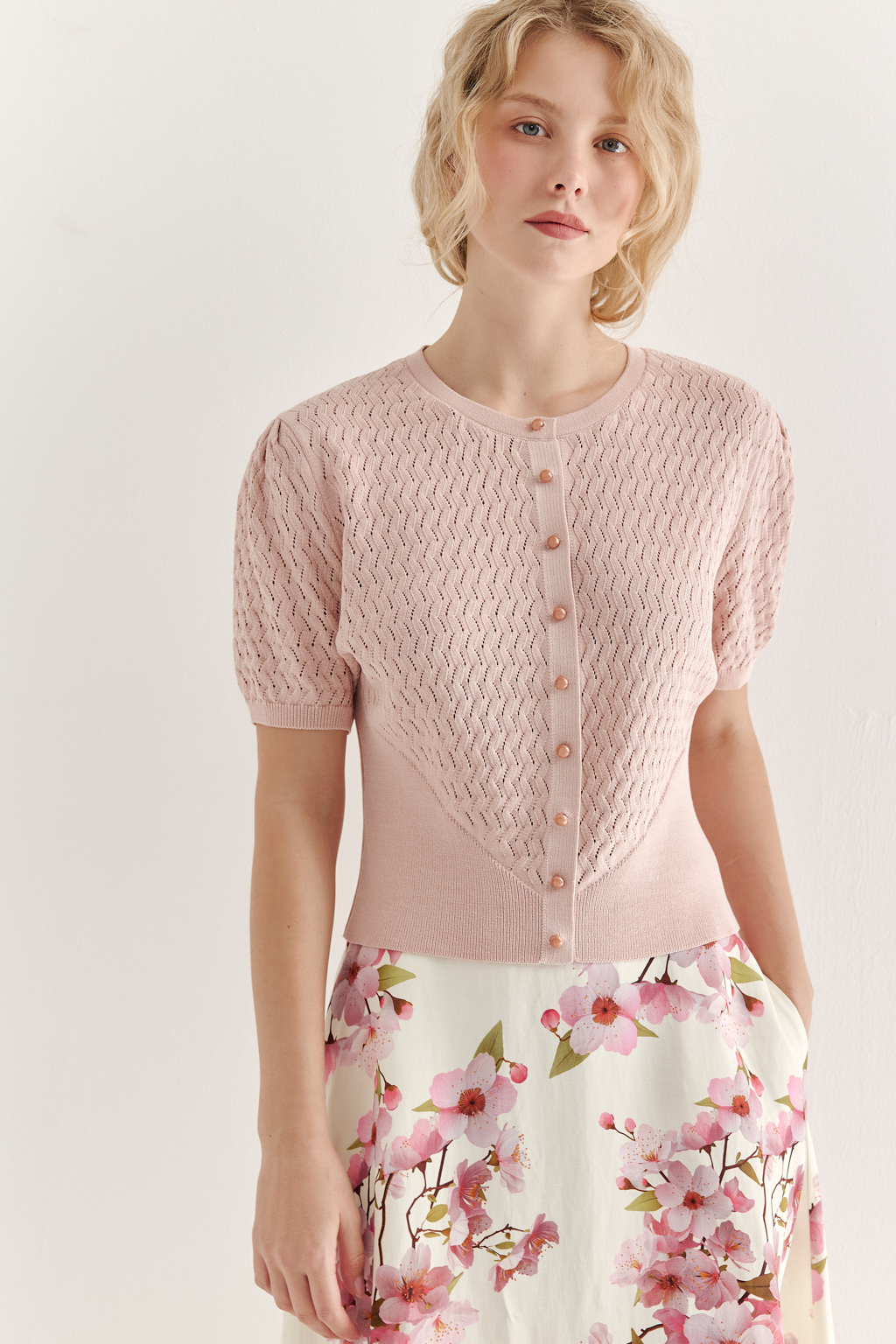 Джемпер нежно-розового цвета, связанный из тонкой тактильной пряжи, в составе которой вискоза и нейлон. В дизайне джемпера применен принцип контраста фактур, в данном случае – полупрозрачного ажура и ластика. Круглая горловина и планка с застежкой на 9 пуговиц-жемчужин, рукав длиной одна вторая.
