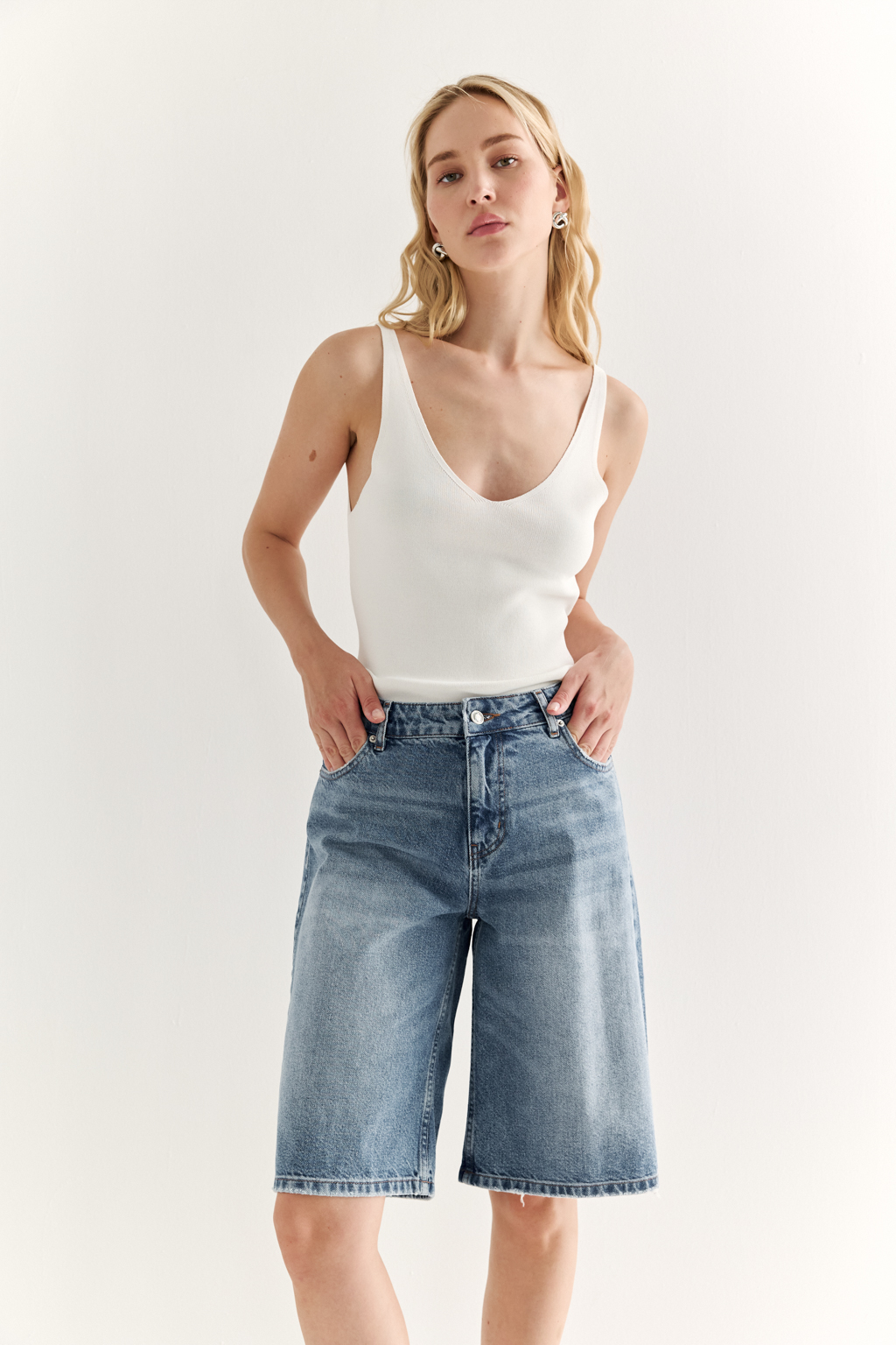 Широкие женские джинсовые шорты ниже колена из легкого денима в синем цвете. Эффект легкой потертости придаст образам расслабленности.