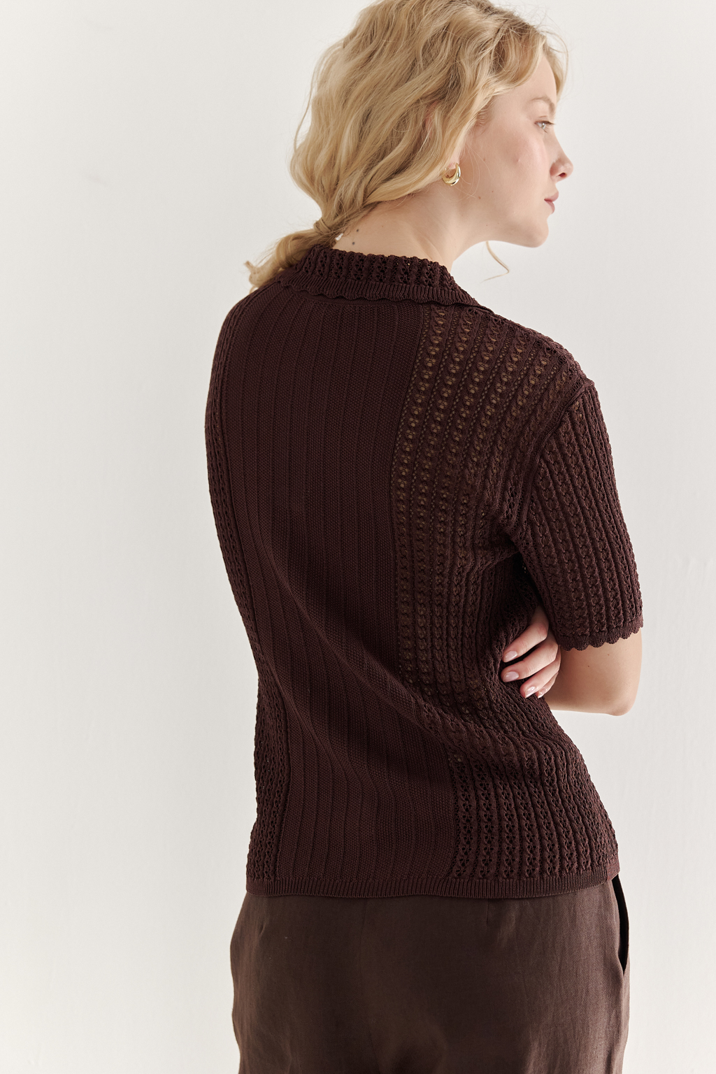 Джемпер-поло шоколадно-коричневого цвета полуприлегающего силуэта средней длины из вискозной пряжи, выполнен в комбинации полупрозрачной сетки и жаккарда, низ рукава и оторочка воротника - изящные фестоны. Рукав короткий, застежка на укороченной планке горловины на три пуговицы.