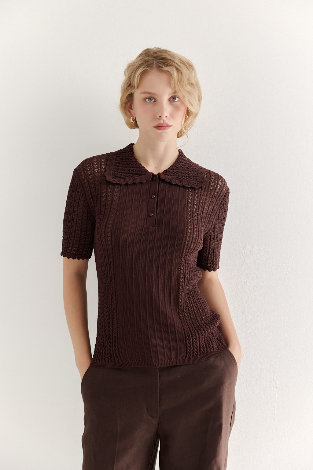 Джемпер-поло шоколадно-коричневого цвета полуприлегающего силуэта средней длины из вискозной пряжи, выполнен в комбинации полупрозрачной сетки и жаккарда, низ рукава и оторочка воротника - изящные фестоны. Рукав короткий, застежка на укороченной планке горловины на три пуговицы.