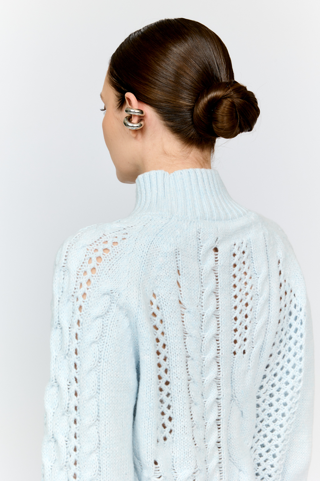 Свитер голубого цвета из мягкой пряжи фигурной вязки с ассиметричными косами, с высокой горловиной и длинным рукавом реглан отлично стилизуется с денимом и обувью на плоском ходу.