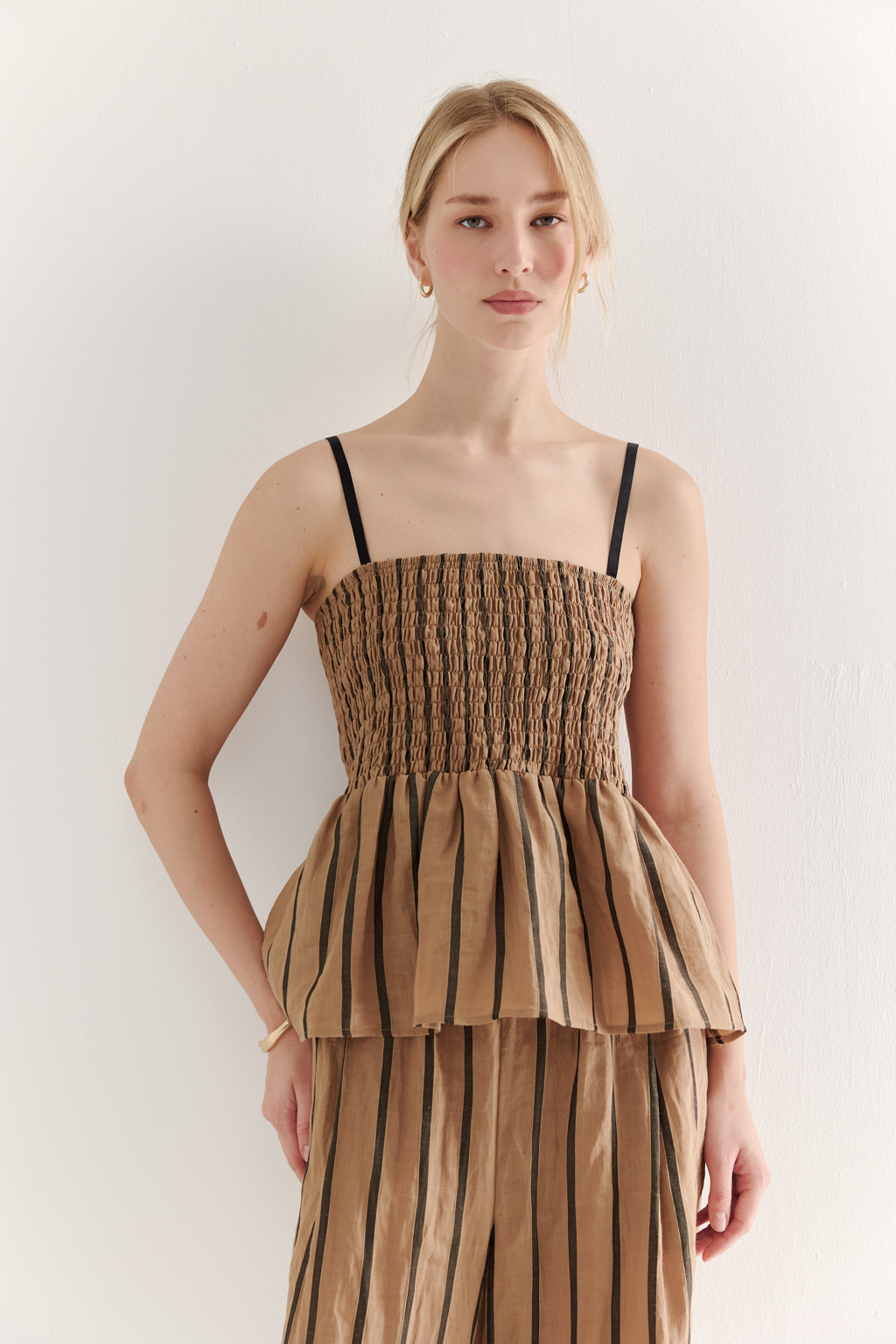 Топ-бандо из эластичных стрейч-нитей, выполненный из платьевой ткани с полской. Состав ткани представляет собой гармоничное сочетание натуральных волокон крапивы и хлопка, обработанных методом растительного окрашивания (natural dye), что обеспечивает экологичность и мягкость материала. Топ состоит из двух основных частей: верхней присборенной бандо-секции и нижней части топа. Поддержка обеспечивается съемными бретелями, которые позволяют варьировать стиль ношения.