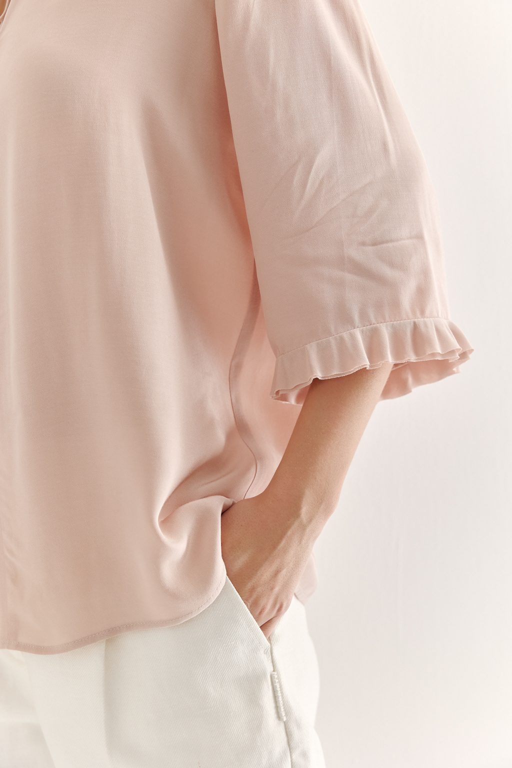 Эта романтичная блуза выполнена из вискозного крепа в нежном пудрово-розовом оттенке. Горловина и рукава украшены изящными рюшами, добавляющими образу легкости и утонченности. Оригинальный разрез спереди кокетливо завязывается на тонкий шнур-рулик и фиксируется воздушной петлей на пуговицу. Прямой силуэт и рукава длиной одна вторая обеспечивают комфорт и свободу движений. Эта блуза — идеальный выбор для создания непринужденных, но элегантных городских образов.