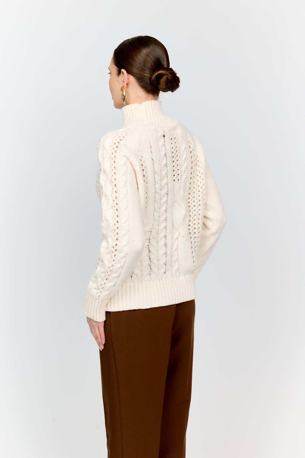 Свитер молочного цвета из мягкой пряжи фигурной вязки с ассиметричными косами, с высокой горловиной и длинным рукавом реглан отлично стилизуется с денимом и обувью на плоском ходу.