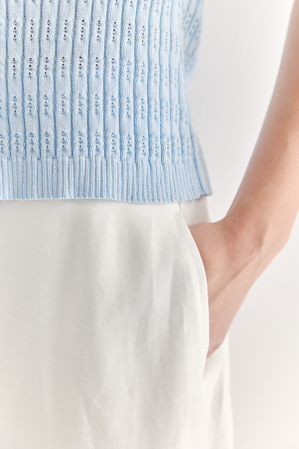 Фактурный топ-майка прилегающего силуэта из вискозной пряжи связана косами, проймы и горловина отделаны вязанными кантами. Цвет – голубой.
