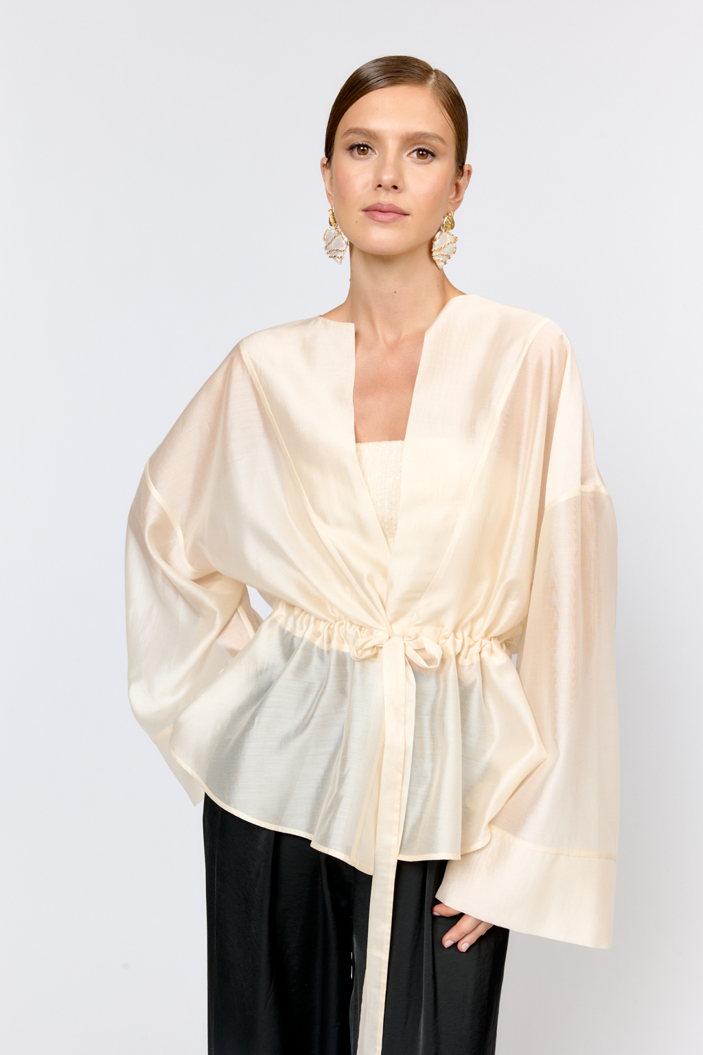 Нарядная блуза из полупрозрачной ткани на кулиске по талии и широкими рукавами большого объема с широкими манжетами по низу дополнит образ с брюками, юбками и платьями в качестве верхнего слоя или в дополнении с топом.  Выполнена из легкой полупрозрачной ткани из тенселя  с содержанием шёлка. Тенсель  -  волокно растительного происхождения, получаемое из древесины эвкалипта по экологически чистому технологическому процессу. Отличается  воздухопроницаемостью и гигроскопичностью.  Шёлк обеспечивает роскошный внешний вид и пластичность ткани.  Преимущества ткани: шелковистая поверхность ткани с жемчужным переливом выглядит премиально и нарядно. Легкая прозрачность делает образ трендовым.