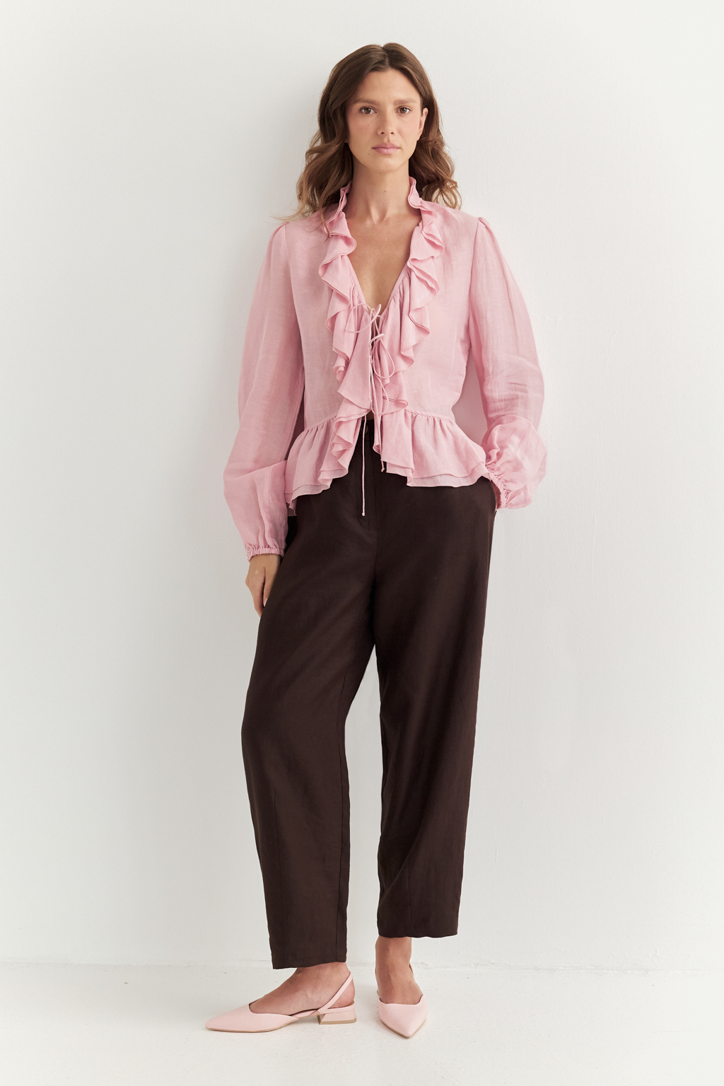 Блуза, выполненная в стиле бохо-шик, предстает в нежном розовом оттенке. Ткань, сотканная из льна и вискозы, дарит ощущение легкости. Рюши изящно обрамляют борт и низ изделия, втачной рукав, слегка расширяющийся книзу, завершается мягким объемным манжетом. Блуза завязывается на шнуры-рулики.  Создавайте из этой блузы романтические образы, используйте ее также как второй слой для  многослойного сложного образа.