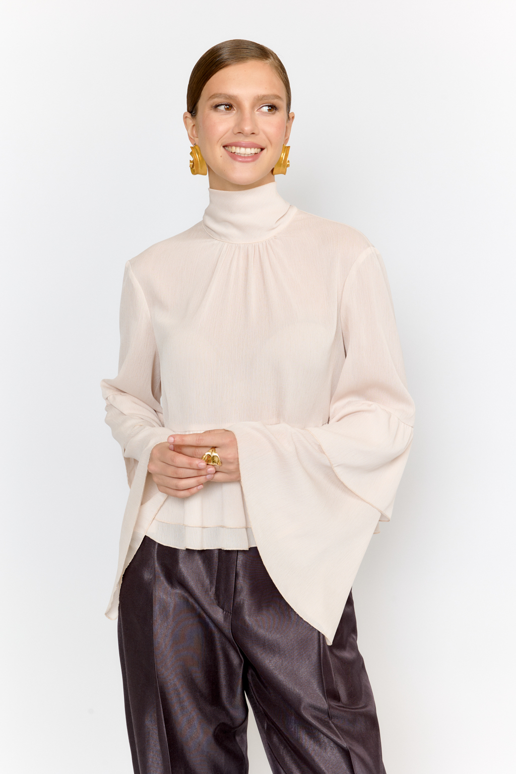 Блуза свободного кроя с легким расширением к низу с воланами и воротником-стойкой, переходящим в ленты, которые можно завязать в бант либо просто перекинуть через плечи. Выполнена из легкой полупрозрачной ткани. Крэш-шифон -легкий, дышащий материал, создающий эффект невесомости. Полиэстеровые волокна в составе обеспечивают   неприхотливость в уходе и устойчивость к механическим повреждениям. Нежный цвет экрю позволяет легко вписать блузу в гардероб, для создания как праздничных образов, так и повседневных.