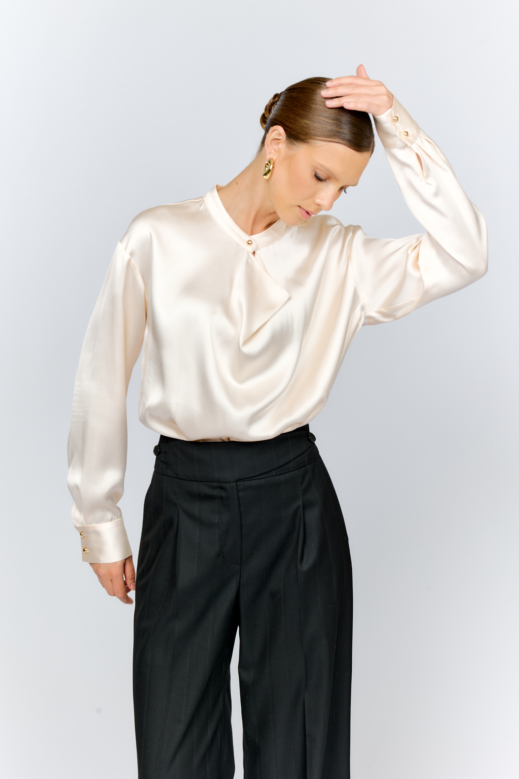 Блуза свободного кроя из шелковистой вискозы с интересной деталью в виде складки на горловине с застежкой на декоративную золотую пуговицу. Изделие придаст стильный акцент к любому образу.