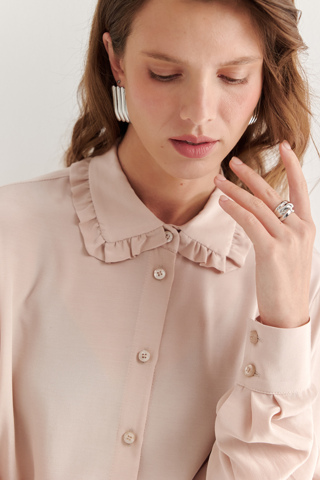 Блуза-батник в нежном пудрово-розовом оттенке станет изысканным дополнением к жакету, брюкам или верхней одежде, позволяя создавать актуальные многослойные образы. Изготовленная из вискозной ткани, она обладает превосходными тактильными качествами и напоминает дорогой шелковый креп. Классическая блузка свободного кроя с отложным воротником и стойкой, украшенной узким рюшем, имеет кокетку спинки, планку для застежки и втачной прямой рукав с манжетой на пуговицах.