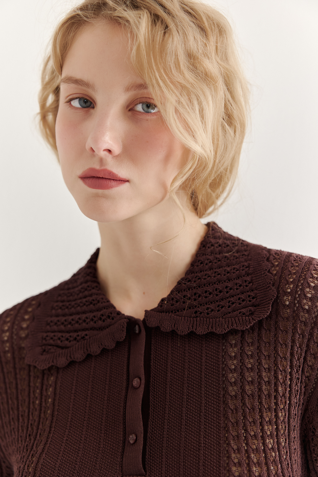 Джемпер-поло шоколадно-коричневого цвета полуприлегающего силуэта средней длины из вискозной пряжи, выполнен в комбинации полупрозрачной сетки и жаккарда, низ рукава и оторочка воротника - изящные фестоны. Рукав короткий, застежка на укороченной планке горловины на три пуговицы.