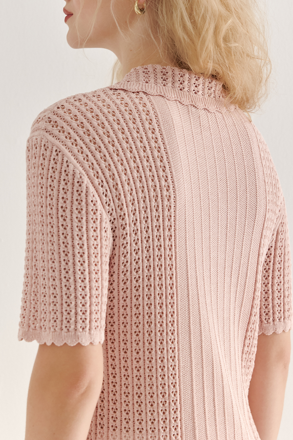 Джемпер-поло нежно-розового цвета полуприлегающего силуэта средней длины из вискозной пряжи, выполнен в комбинации полупрозрачной сетки и жаккарда, низ рукава и оторочка воротника - изящные фестоны. Рукав короткий, застежка на укороченной планке горловины на три пуговицы.