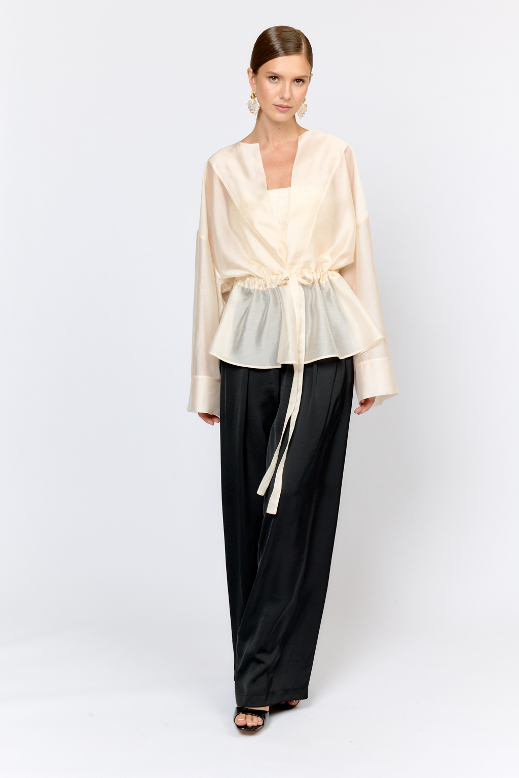 Нарядная блуза из полупрозрачной ткани на кулиске по талии и широкими рукавами большого объема с широкими манжетами по низу дополнит образ с брюками, юбками и платьями в качестве верхнего слоя или в дополнении с топом.  Выполнена из легкой полупрозрачной ткани из тенселя  с содержанием шёлка. Тенсель  -  волокно растительного происхождения, получаемое из древесины эвкалипта по экологически чистому технологическому процессу. Отличается  воздухопроницаемостью и гигроскопичностью.  Шёлк обеспечивает роскошный внешний вид и пластичность ткани.  Преимущества ткани: шелковистая поверхность ткани с жемчужным переливом выглядит премиально и нарядно. Легкая прозрачность делает образ трендовым.