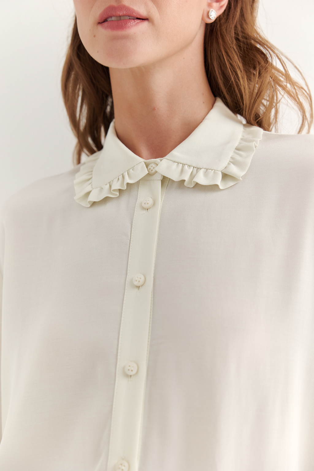 Блуза-батник в нежном оттенке сливочное масло станет изысканным дополнением к жакету, брюкам или верхней одежде, позволяя создавать актуальные многослойные образы. Изготовленная из вискозной ткани, она обладает превосходными тактильными качествами и напоминает дорогой шелковый креп. Классическая блузка свободного кроя с отложным воротником и стойкой, украшенной узким рюшем, имеет планку для застежки и втачной прямой рукав с манжетой на пуговицах.