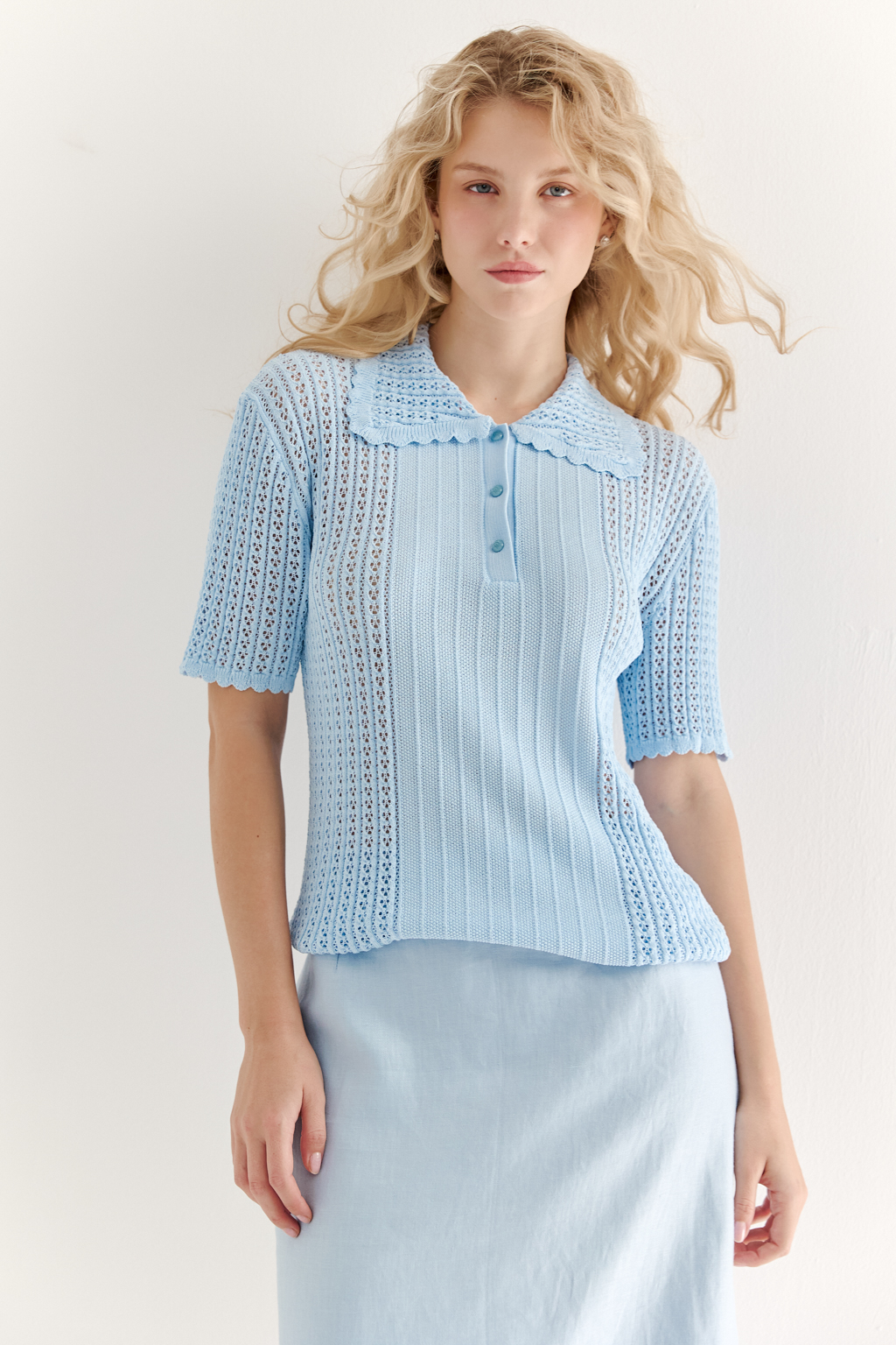 Джемпер-поло нежно-голубого цвета полуприлегающего силуэта средней длины из вискозной пряжи, выполнен в комбинации полупрозрачной сетки и жаккарда, низ рукава и оторочка воротника - изящные фестоны. Рукав короткий, застежка на укороченной планке горловины на три пуговицы.