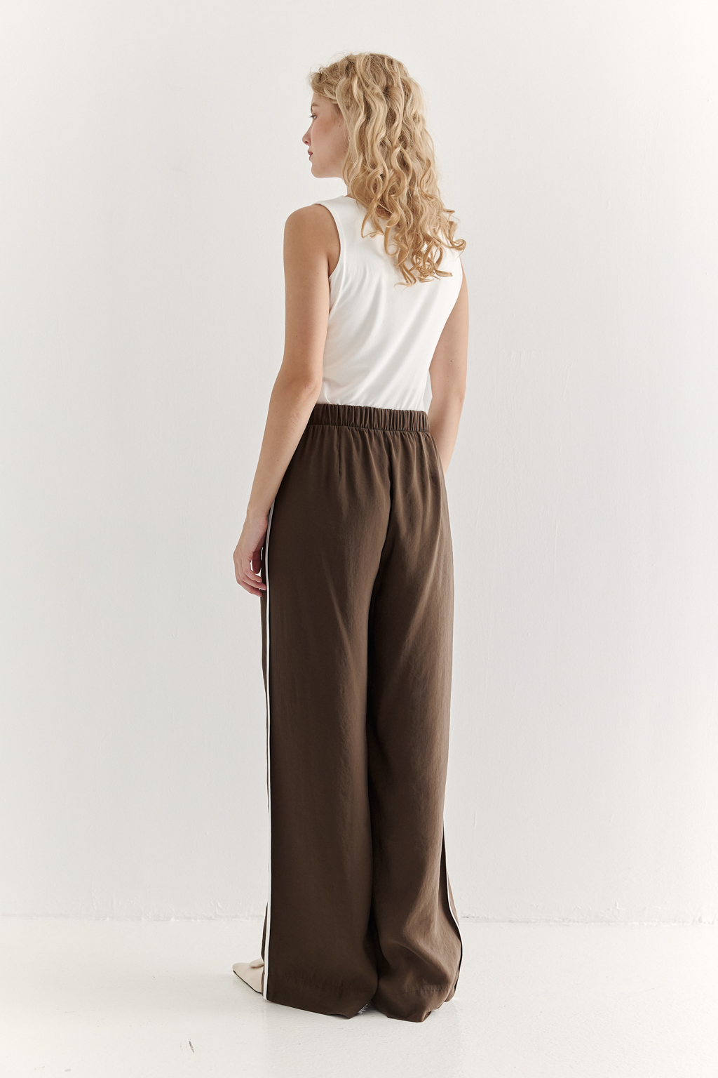Эти широкие брюки свободного кроя, выполненные из мягкого модала насыщенного шоколадно-коричневого оттенка. Бархатистая текстура ткани, созданная благодаря особой обработке, дарит неповторимое ощущение нежности, тактильно напоминая прикосновение к кожице спелого персика – тот самый «Peach эффект». Боковые швы брюк обработаны шелковистым кантом молочного цвета. Эластичный пояс и удобные боковые карманы обеспечивают исключительный комфорт. Брюки идеально сочетаются с блузой из аналогичной ткани, создавая гармоничный ансамбль, а также с компактными трикотажными блузами и топами светлых оттенков, позволяя создавать множество стильных образов.