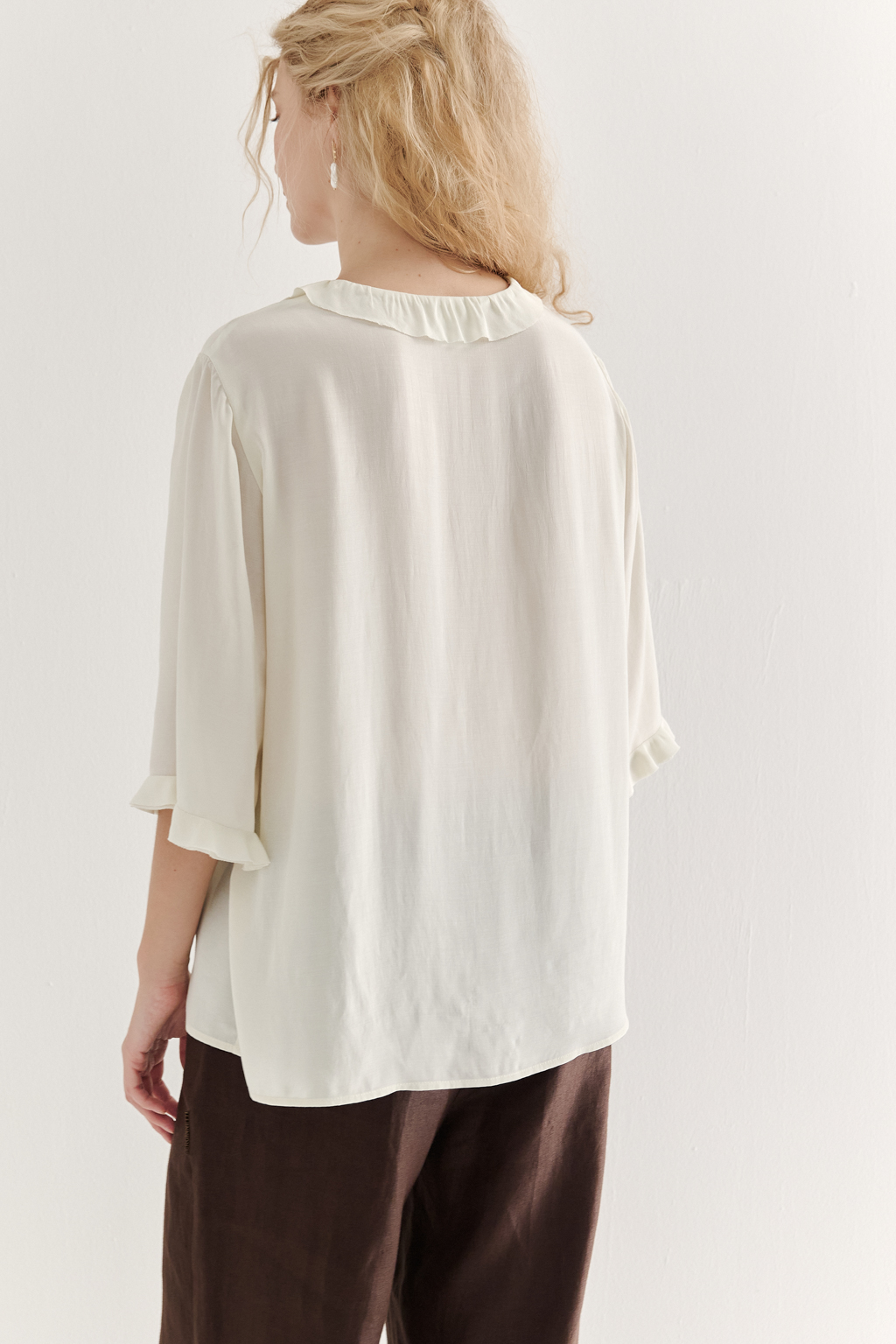 Эта романтичная блуза выполнена из вискозного крепа в нежном оттенке словочное масло. Горловина и рукава украшены изящными рюшами, добавляющими образу легкости и утонченности. Оригинальный разрез спереди кокетливо завязывается на тонкий шнур-рулик и фиксируется воздушной петлей на пуговицу. Прямой силуэт и рукава длиной одна вторая обеспечивают комфорт и свободу движений. Эта блуза — идеальный выбор для создания непринужденных, но элегантных городских образов.