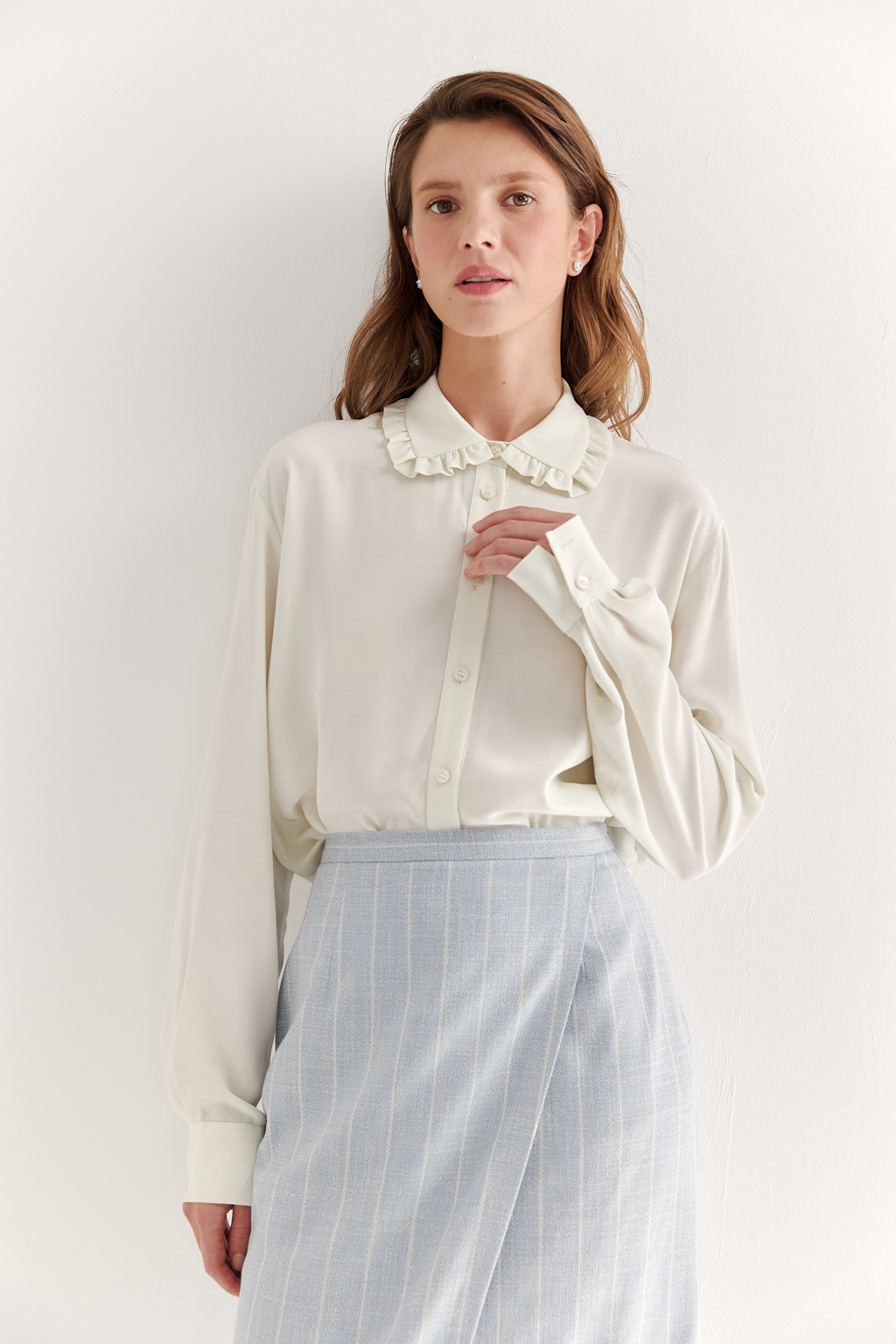 Блуза-батник в нежном оттенке сливочное масло станет изысканным дополнением к жакету, брюкам или верхней одежде, позволяя создавать актуальные многослойные образы. Изготовленная из вискозной ткани, она обладает превосходными тактильными качествами и напоминает дорогой шелковый креп. Классическая блузка свободного кроя с отложным воротником и стойкой, украшенной узким рюшем, имеет планку для застежки и втачной прямой рукав с манжетой на пуговицах.