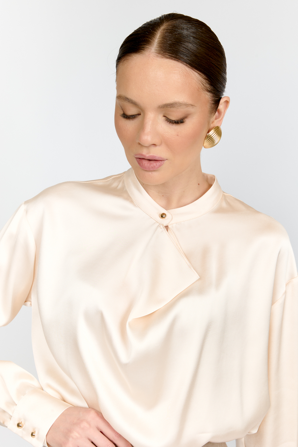 Блуза свободного кроя из шелковистой вискозы с интересной деталью в виде складки на горловине с застежкой на декоративную золотую пуговицу. Изделие придаст стильный акцент к любому образу.