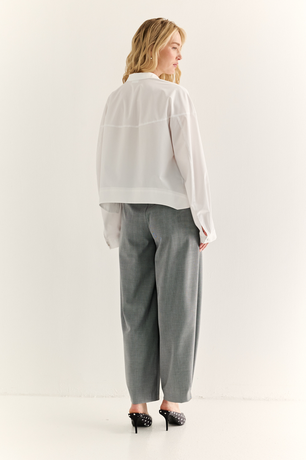 Oversize-рубашка с кокеткой: объём как способ выразить себя. Эта укороченная рубашка с удлинённой кокеткой и объёмными рукавами — модный акцент, который задаёт ритм всему образу. Мягко закруглённый низ подчёркивает талию и визуально вытягивает силуэт, а объёмный крой создаёт эффект расслабленного шика. Широкая кокетка, фактурные швы и сборка по рукавам добавляют архитектурности и свежести классической рубашке. Застёжка на пуговицы и аккуратный воротник сохраняют баланс между формальностью и актуальностью. Новая форма свободы — уверенная, воздушная, выразительная.