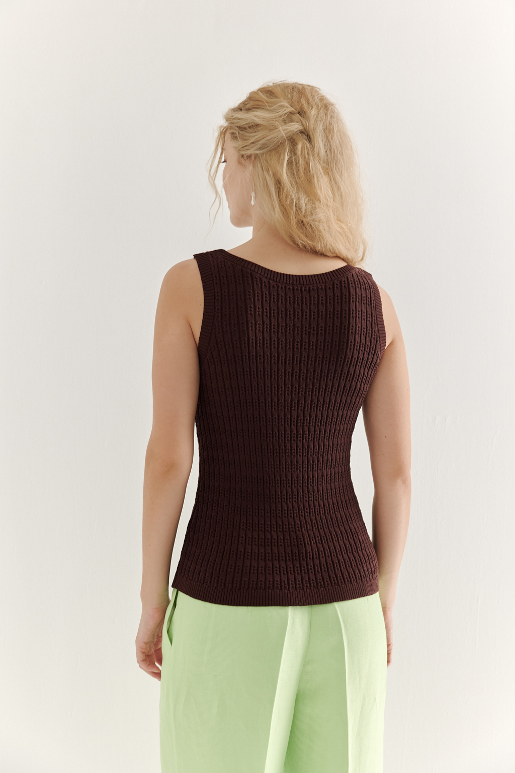 Фактурный топ-майка прилегающего силуэта из вискозной пряжи связана косами, проймы и горловина отделаны вязанными кантами. Цвет – шоколадно-коричневый.