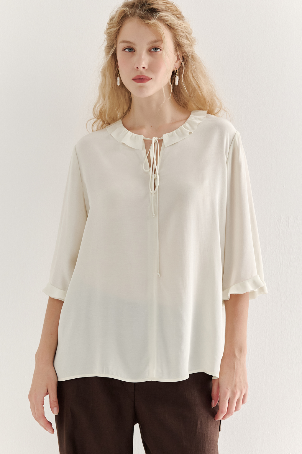 Эта романтичная блуза выполнена из вискозного крепа в нежном оттенке словочное масло. Горловина и рукава украшены изящными рюшами, добавляющими образу легкости и утонченности. Оригинальный разрез спереди кокетливо завязывается на тонкий шнур-рулик и фиксируется воздушной петлей на пуговицу. Прямой силуэт и рукава длиной одна вторая обеспечивают комфорт и свободу движений. Эта блуза — идеальный выбор для создания непринужденных, но элегантных городских образов.