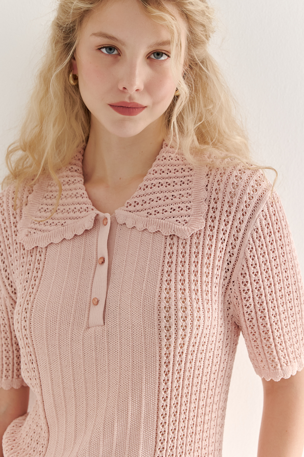 Джемпер-поло нежно-розового цвета полуприлегающего силуэта средней длины из вискозной пряжи, выполнен в комбинации полупрозрачной сетки и жаккарда, низ рукава и оторочка воротника - изящные фестоны. Рукав короткий, застежка на укороченной планке горловины на три пуговицы.