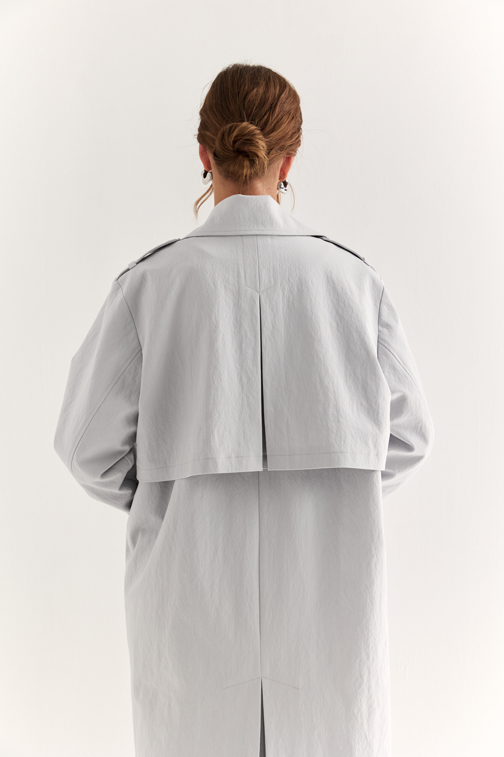 Плащ двубортный прямого силуэта длиной макси с расширенной линией плеча и отлётными кокетками по полочке и спинке. Приталивается завязывающимся поясом.