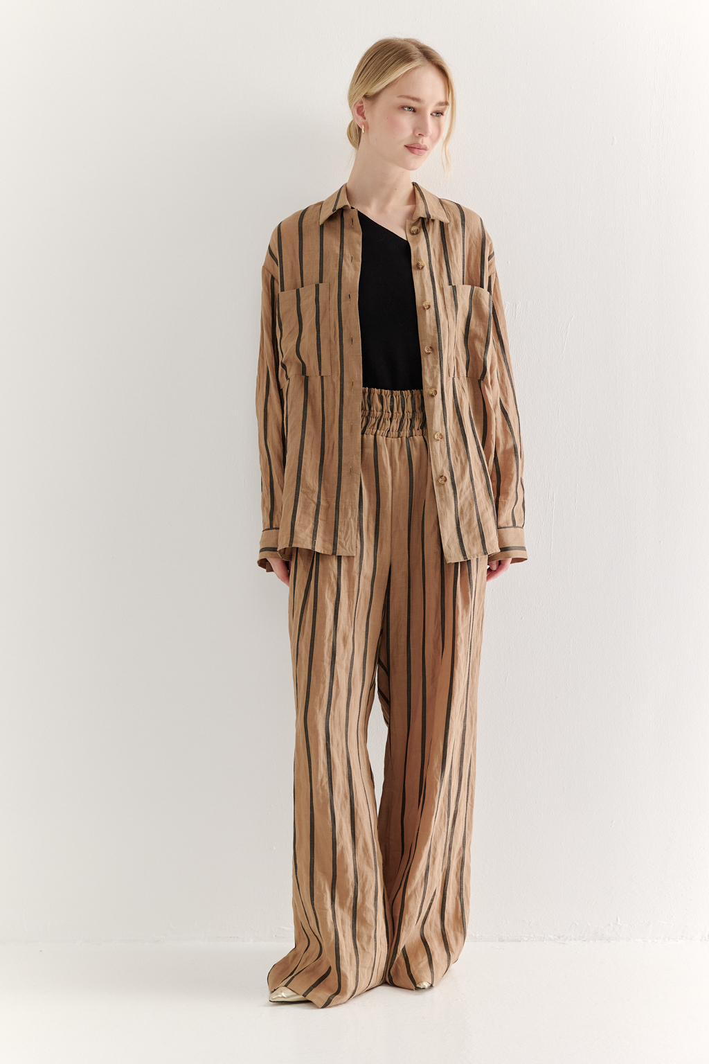 Блуза-рубашка свободного кроя изготовлена сшиты из ткани в темную полоску на песочном фоне. Ткань сочетает в себе волокна крапивы и хлопка, прошедшие обработку с использованием натуральных красителей (natural dye). Дизайн, вдохновлённый классической мужской рубашкой, включает в себя воротник-стойку, планку с застёжкой и длинные рукава с манжетами. Свободный расслабленный стиль рубашки идеально рифмуется с комфортными брюками из этой же ткани и компактными трикотажными джемперами и топами. Яркое решение образа создает комфортный и запоминающийся образ