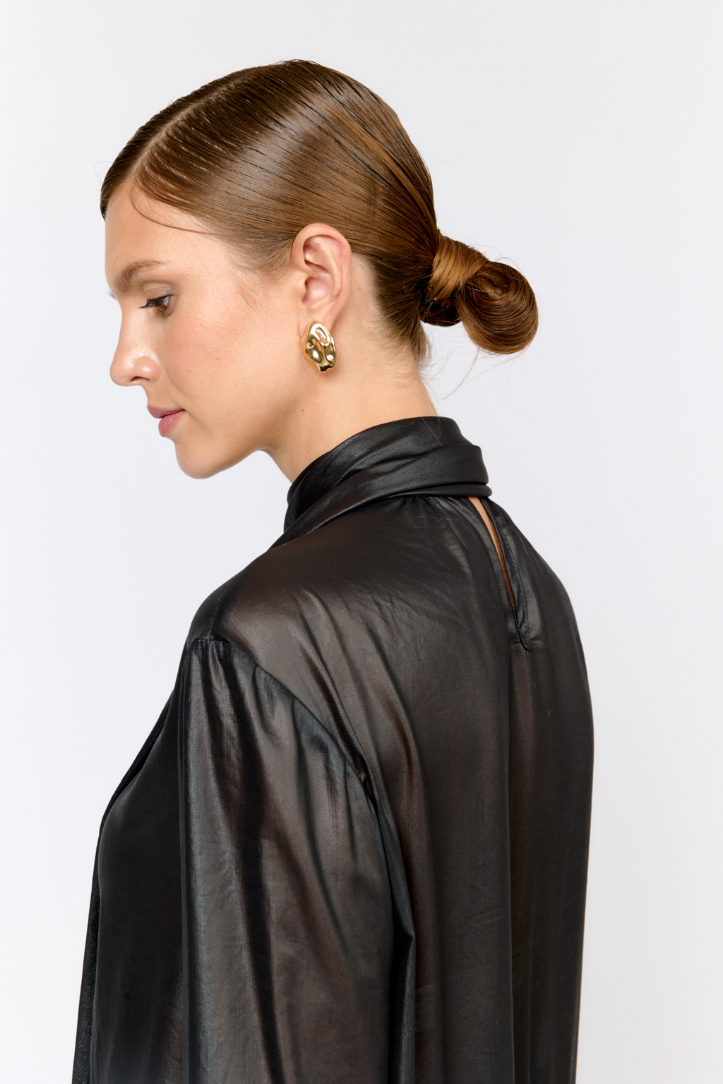 Блуза свободного кроя с летим расширением книзу с воланами по низу и воротником-стойкой, переходящим в ленты, которые можно завязать в бант либо просто перекинуть через плечи. Выполнена из легкой полупрозрачной ткани с глянцевым напылением, создающим эффект кожи. Полиэстер легкий и воздушный материал, создающий ощущение невесомости, практичен в уходе,  устойчив к сминанию. Преимущества ткани: высокотехнологичный материал премиального качества с оригинальным напылением, имитирующим кожу. Ткань пластично драпируется и красиво движется. Приглушенный блеск придает образу нарядность, а необычная фактура делает его стильным.