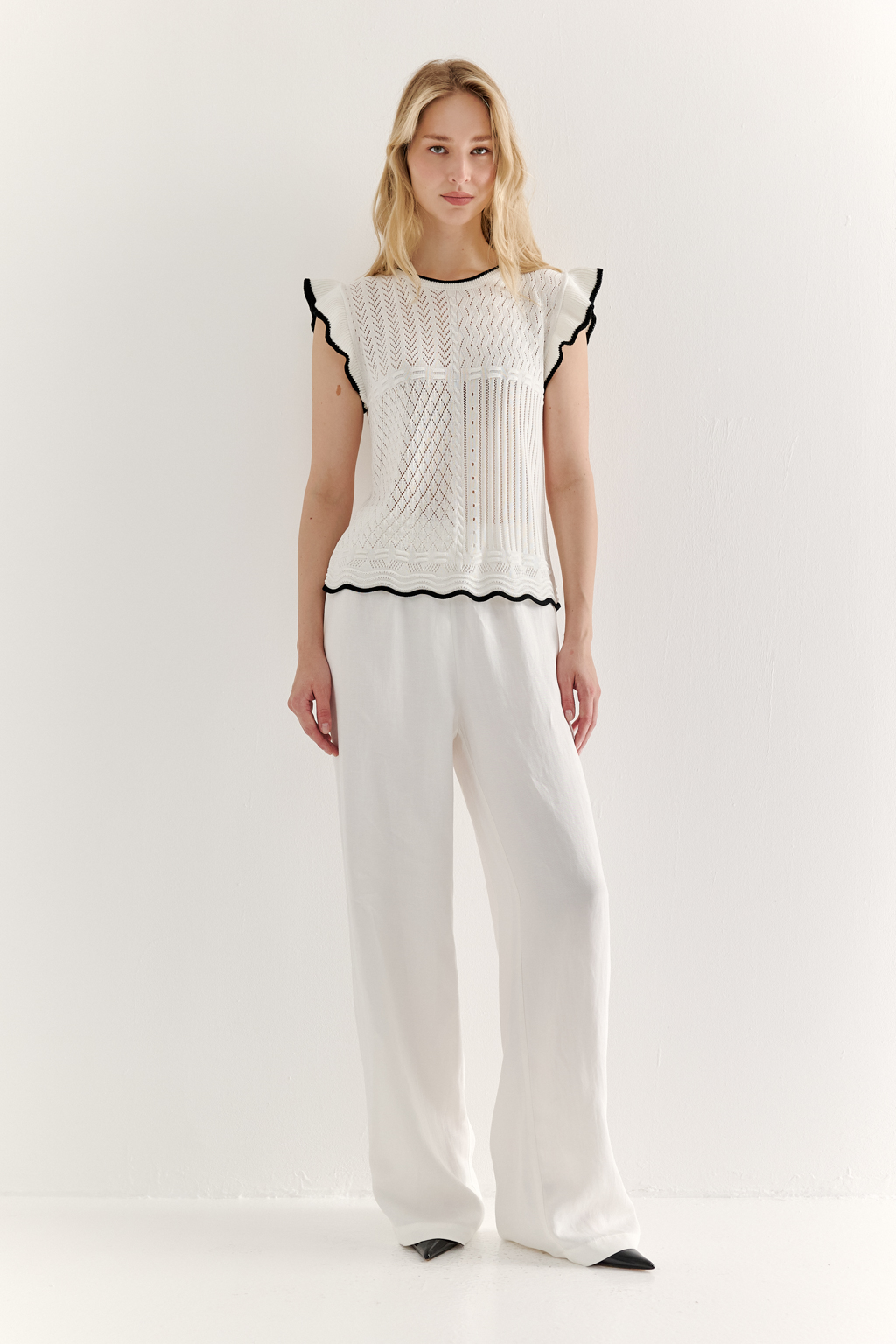 Белый топ, в котором соединились четыре техники ажурной вязки, круглая горловина и деликатные рюши по пройме. Контрастная отделка расположена по линиям горловины, низа и краю рюши.