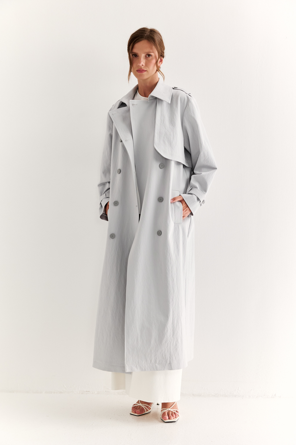 Плащ двубортный прямого силуэта длиной макси с расширенной линией плеча и отлётными кокетками по полочке и спинке. Приталивается завязывающимся поясом.