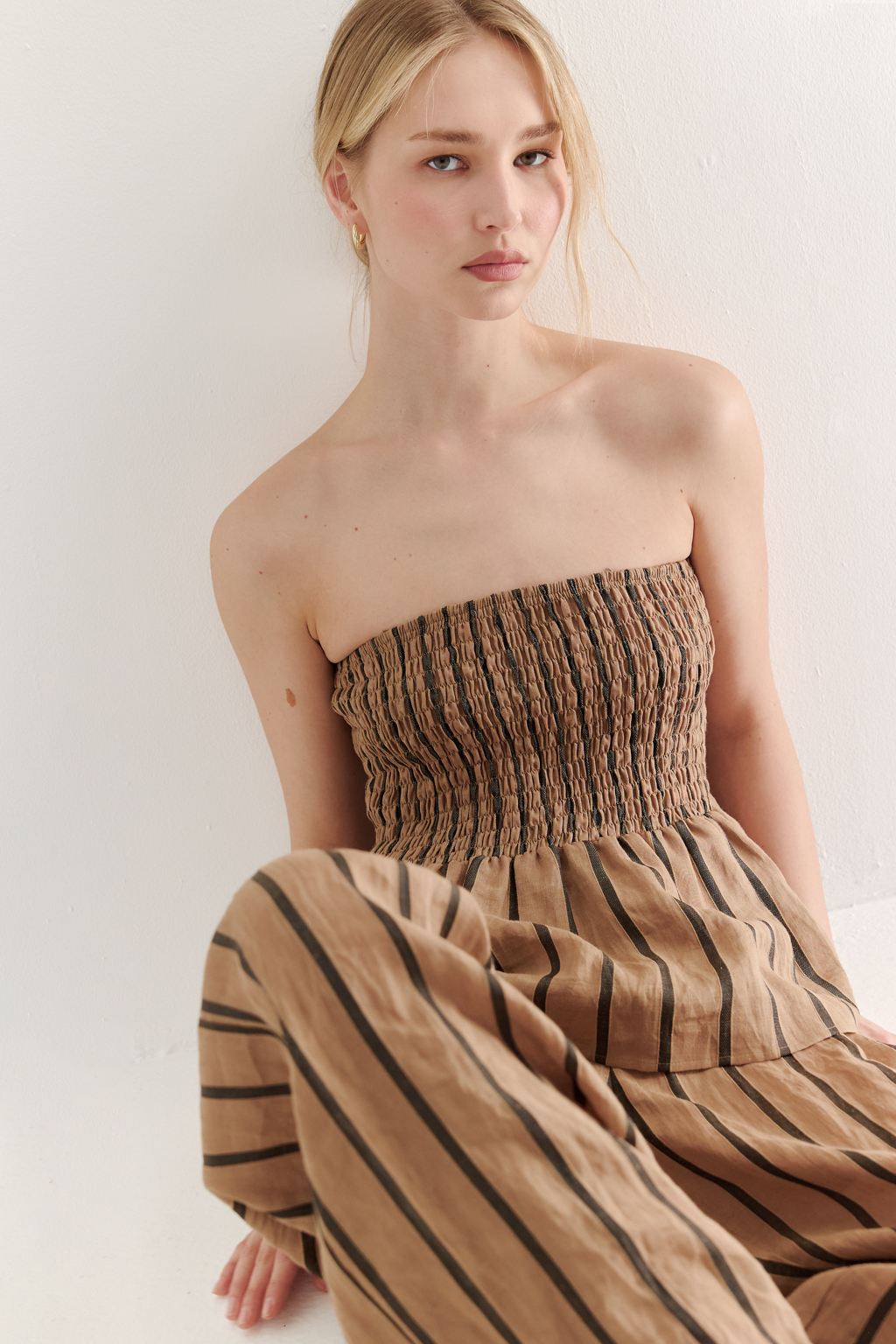 Топ-бандо из эластичных стрейч-нитей, выполненный из платьевой ткани с полской. Состав ткани представляет собой гармоничное сочетание натуральных волокон крапивы и хлопка, обработанных методом растительного окрашивания (natural dye), что обеспечивает экологичность и мягкость материала. Топ состоит из двух основных частей: верхней присборенной бандо-секции и нижней части топа. Поддержка обеспечивается съемными бретелями, которые позволяют варьировать стиль ношения.