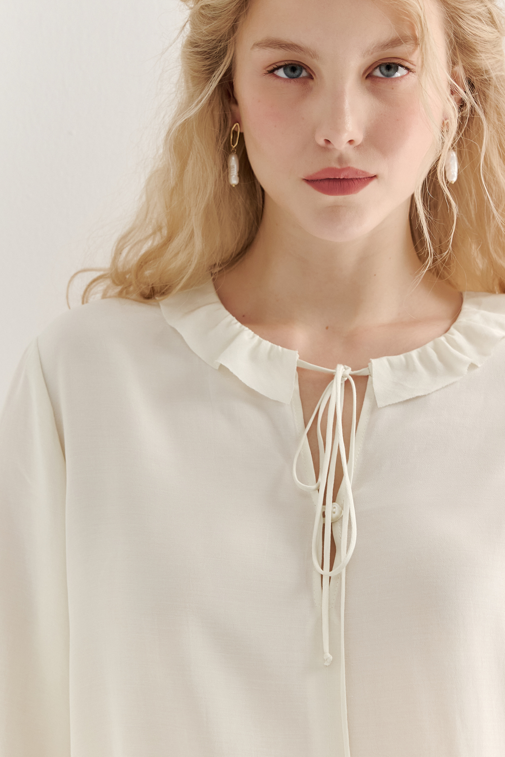 Эта романтичная блуза выполнена из вискозного крепа в нежном оттенке словочное масло. Горловина и рукава украшены изящными рюшами, добавляющими образу легкости и утонченности. Оригинальный разрез спереди кокетливо завязывается на тонкий шнур-рулик и фиксируется воздушной петлей на пуговицу. Прямой силуэт и рукава длиной одна вторая обеспечивают комфорт и свободу движений. Эта блуза — идеальный выбор для создания непринужденных, но элегантных городских образов.