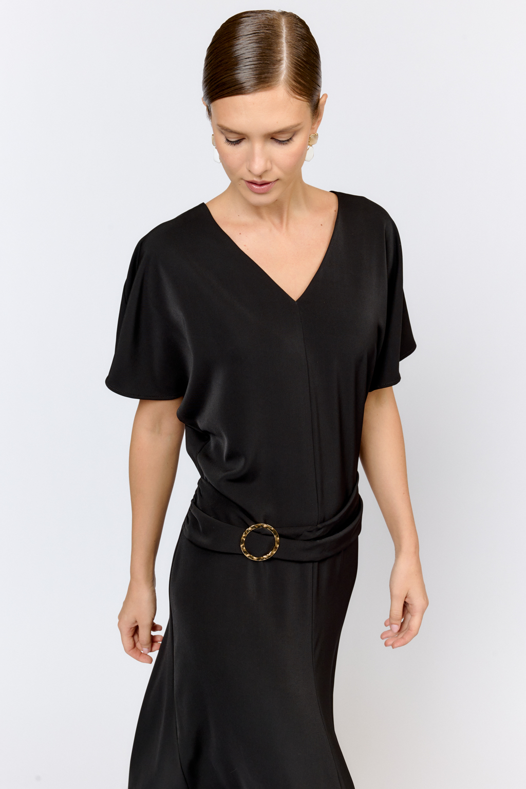 Струящееся платье свободного кроя с цельнокроеными рукавами и открытой горловиной с V-образным вырезом горловины. Модель с декоративной пряжкой на притачном поясе со сборкой по бокам. Выполнено из эластичной плательной ткани. Полиэстер придает ткани устойчивость к сминанию и хорошо держит форму. Что позволяет изделию сохранять опрятный вид в течении дня.  Глубокий черный цвет не тускнеет после стирки. Спандекс добавляет эластичность, обеспечивая идеальную посадку по фигуре. Преимущества ткани: новое современное качество с мягким блеском и благородной фактурой. Ткань легкая, приятна к телу, красиво драпируется при движении. Глубокий черный оттенок придает изделию благородный вид.
