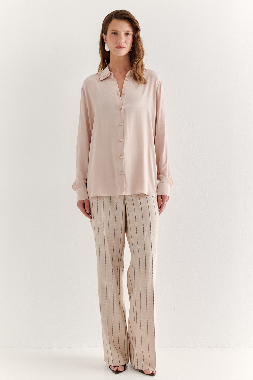 Блуза-батник в нежном пудрово-розовом оттенке станет изысканным дополнением к жакету, брюкам или верхней одежде, позволяя создавать актуальные многослойные образы. Изготовленная из вискозной ткани, она обладает превосходными тактильными качествами и напоминает дорогой шелковый креп. Классическая блузка свободного кроя с отложным воротником и стойкой, украшенной узким рюшем, имеет кокетку спинки, планку для застежки и втачной прямой рукав с манжетой на пуговицах.