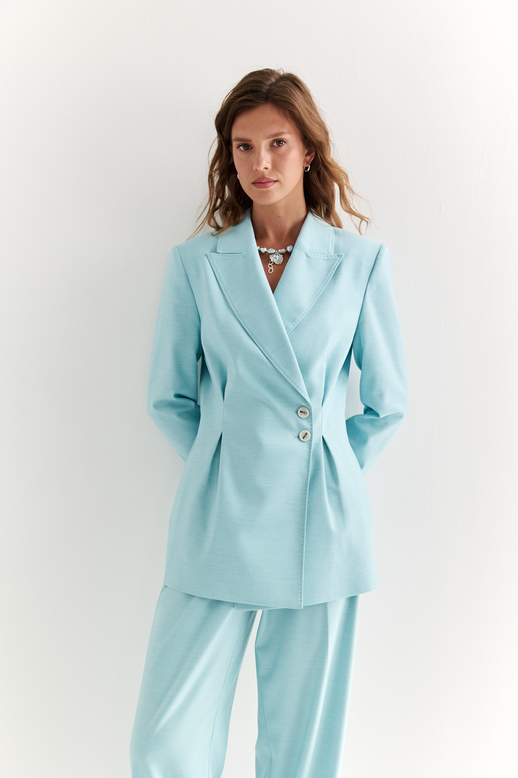 Приталенный жакет: акцент на силуэт и уверенность. Классический жакет со смещённой застёжкой и декоративными складками, подчёркивающими талию, — это вещь, которая формирует образ с первого взгляда. Чёткие линии плеч, заострённые лацканы и приталенный крой создают силуэт, говорящий о силе, вкусе и уверенности. Асимметричная застёжка добавляет изящную детализацию, а универсальная длина делает модель уместной как в деловом комплекте, так и в стилизациях с джинсами или платьями. Идеально садится и подчёркивает фигуру. Современная классика для женщины, которая знает, чего хочет.