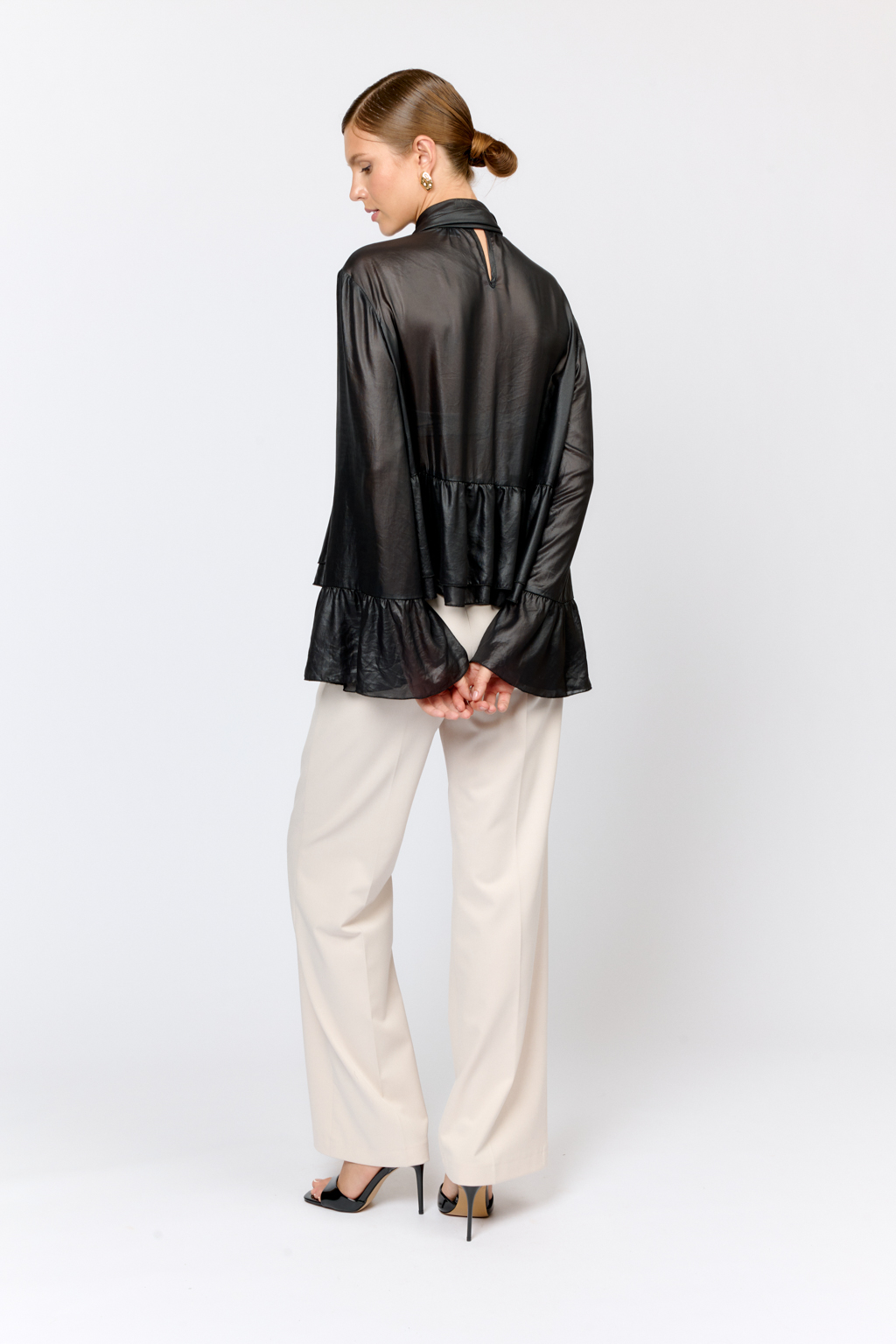 Блуза свободного кроя с летим расширением книзу с воланами по низу и воротником-стойкой, переходящим в ленты, которые можно завязать в бант либо просто перекинуть через плечи. Выполнена из легкой полупрозрачной ткани с глянцевым напылением, создающим эффект кожи. Полиэстер легкий и воздушный материал, создающий ощущение невесомости, практичен в уходе,  устойчив к сминанию. Преимущества ткани: высокотехнологичный материал премиального качества с оригинальным напылением, имитирующим кожу. Ткань пластично драпируется и красиво движется. Приглушенный блеск придает образу нарядность, а необычная фактура делает его стильным.