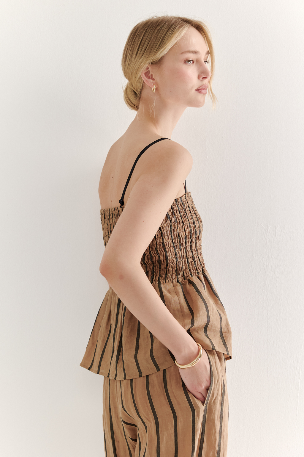 Топ-бандо из эластичных стрейч-нитей, выполненный из платьевой ткани с полской. Состав ткани представляет собой гармоничное сочетание натуральных волокон крапивы и хлопка, обработанных методом растительного окрашивания (natural dye), что обеспечивает экологичность и мягкость материала. Топ состоит из двух основных частей: верхней присборенной бандо-секции и нижней части топа. Поддержка обеспечивается съемными бретелями, которые позволяют варьировать стиль ношения.