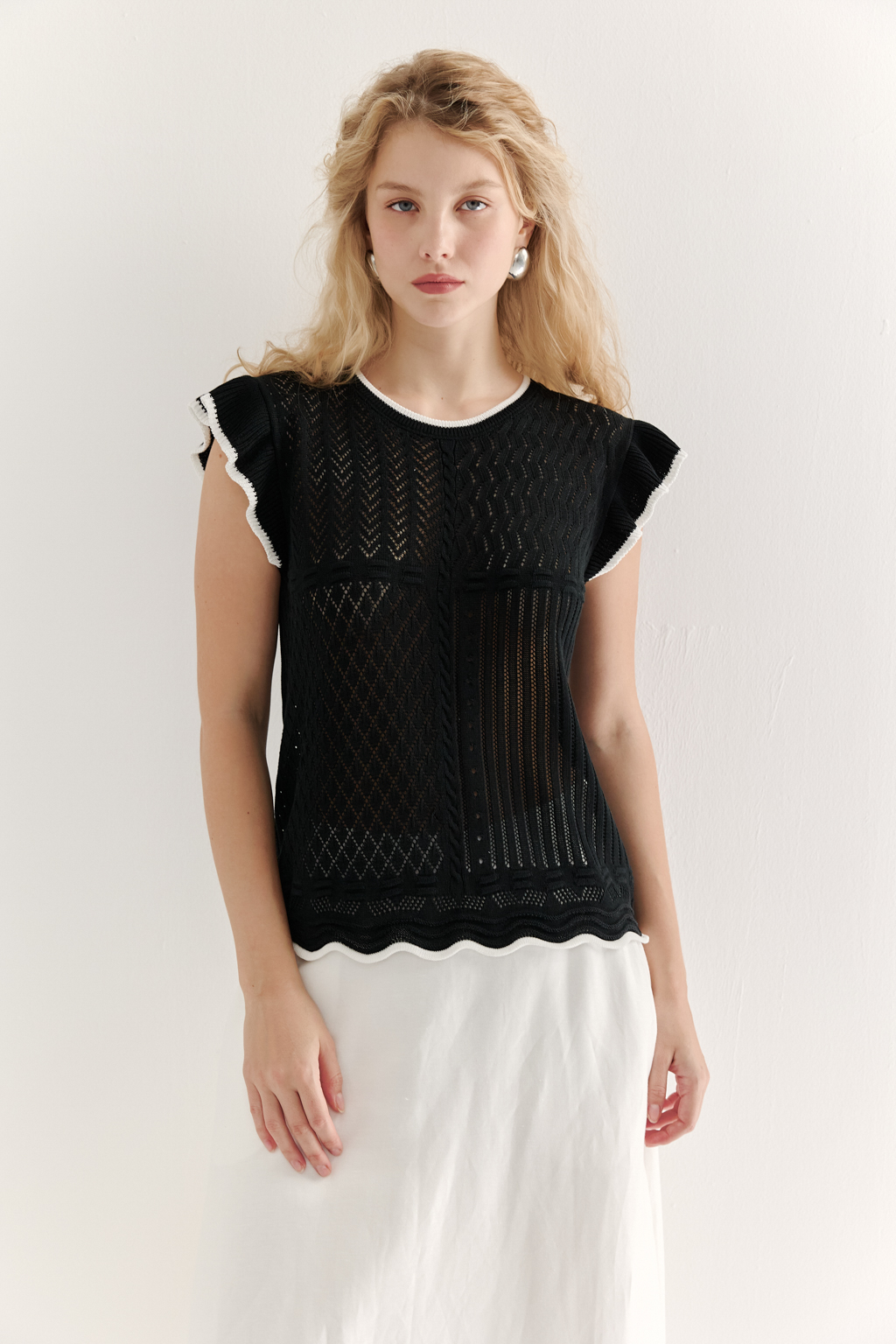 Черный топ в стиле пэчворк, в котором соединились четыре техники ажурной вязки, круглая горловина и деликатные рюши по пройме. Контрастная отделка расположена по линиям горловины, низа и краю рюши.
